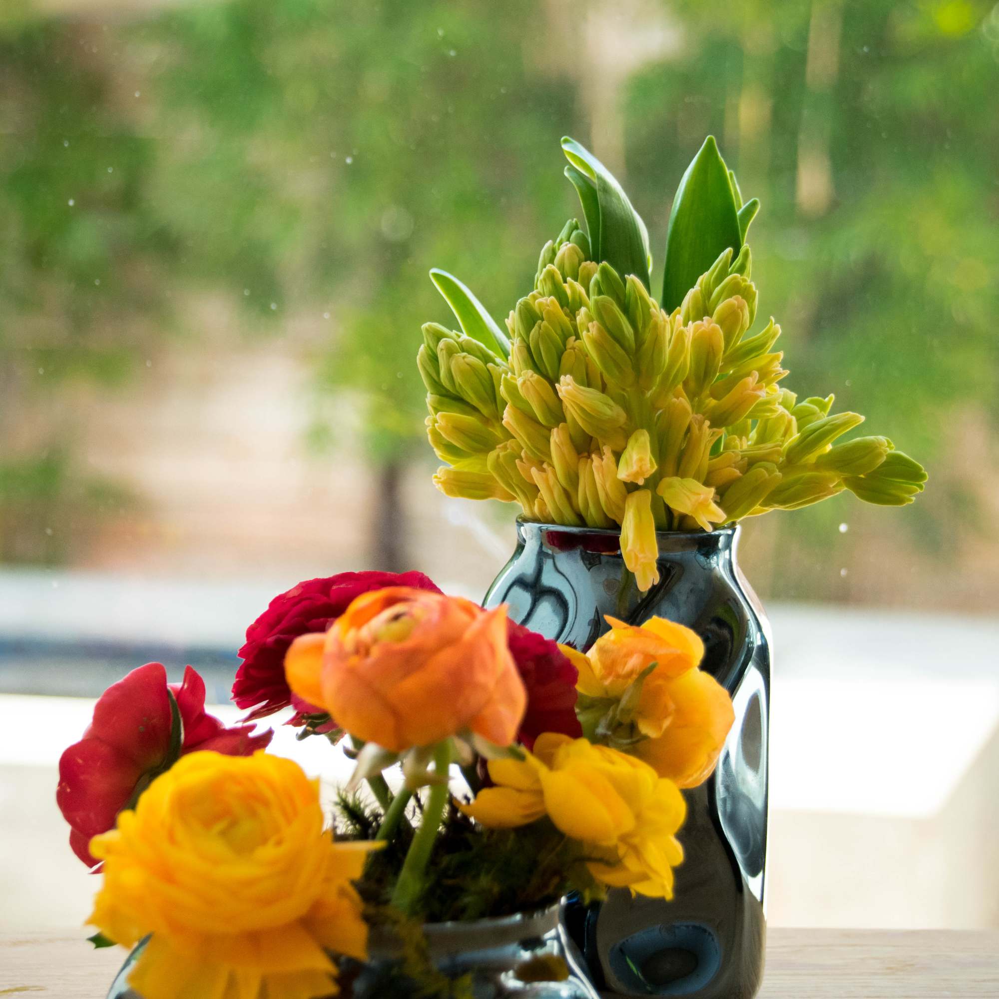 Two small flower arrangements in dark ceramic vases on a wooden table