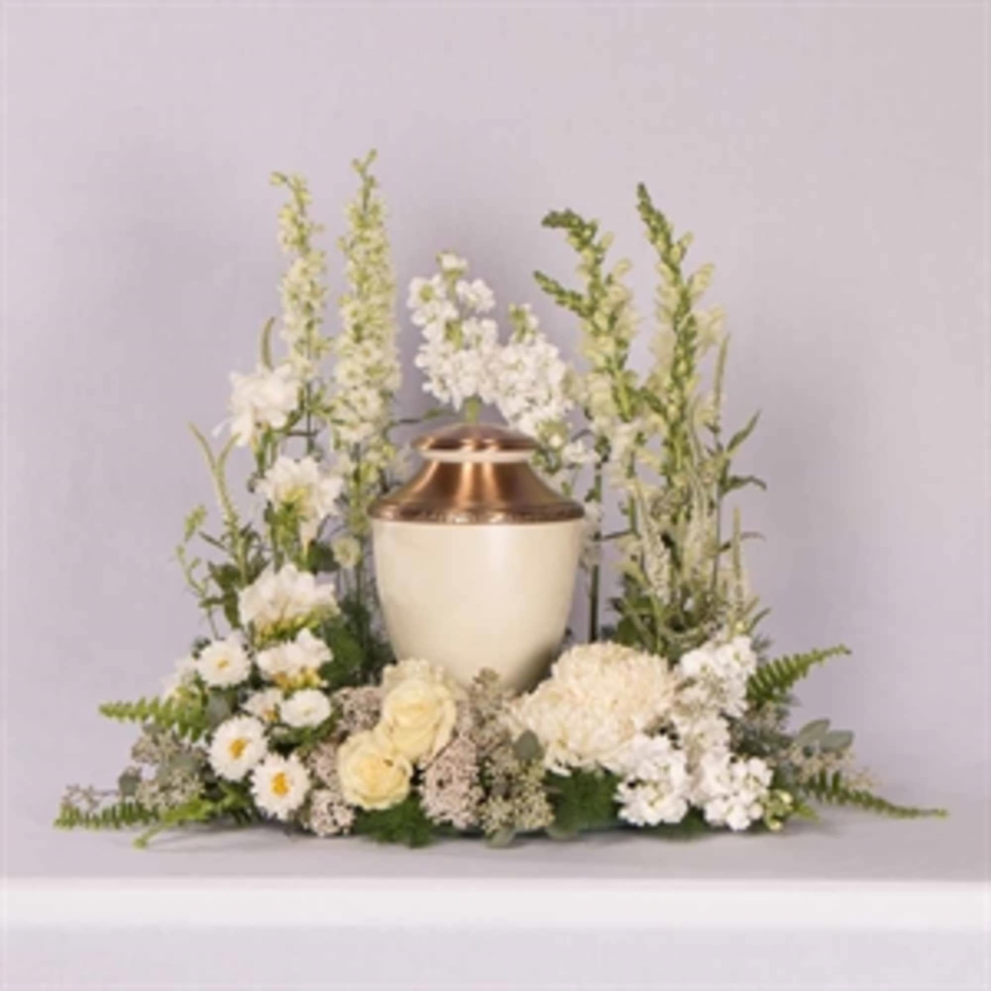 White floral funeral urn arrangement with tall blooms and a copper urn