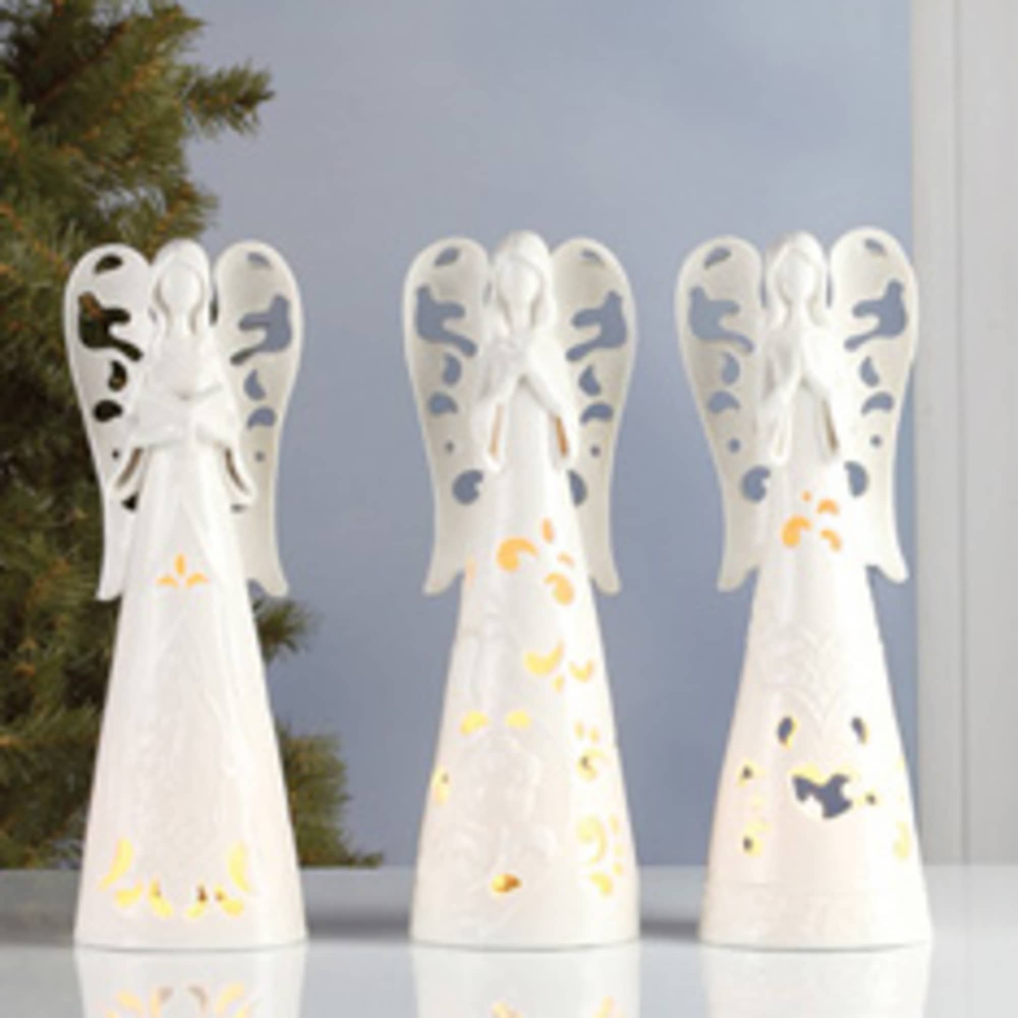 Three white angel figurines with painted accents on a reflective surface