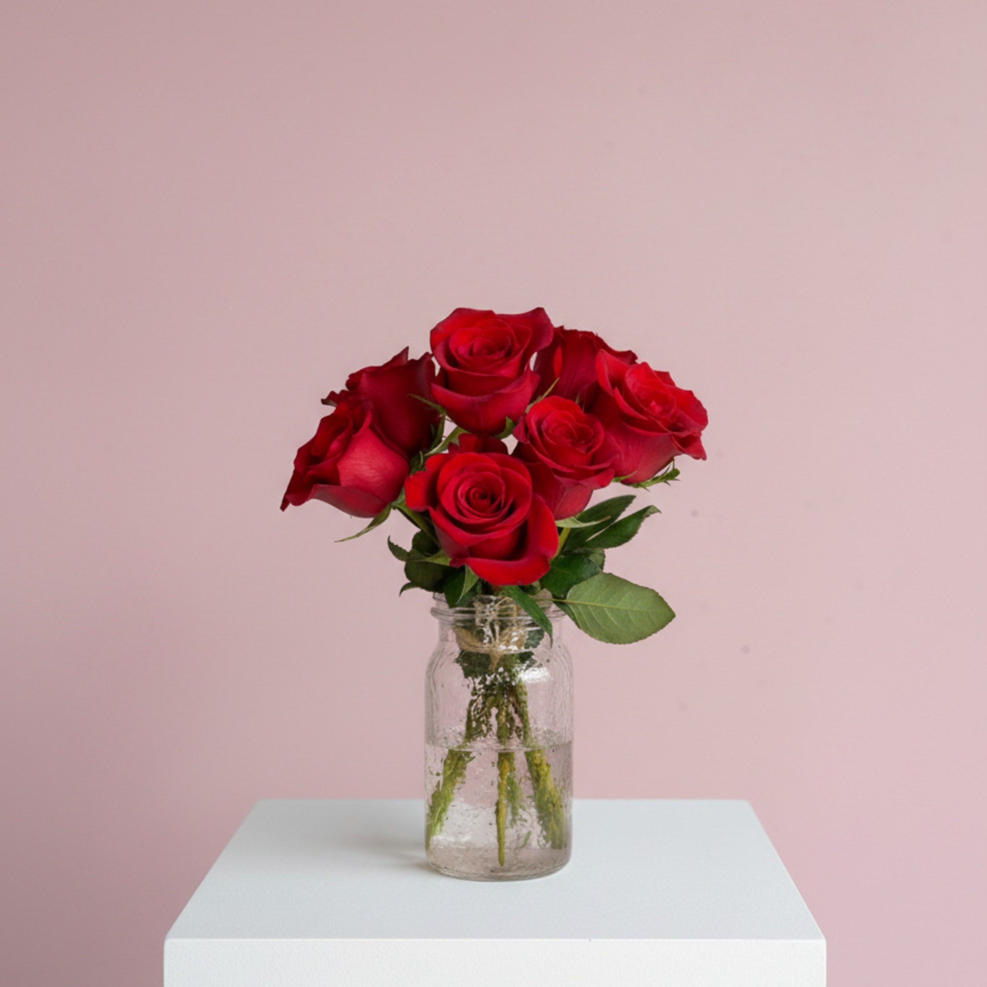 Red roses in a clear glass jar vase on a white pedestal
