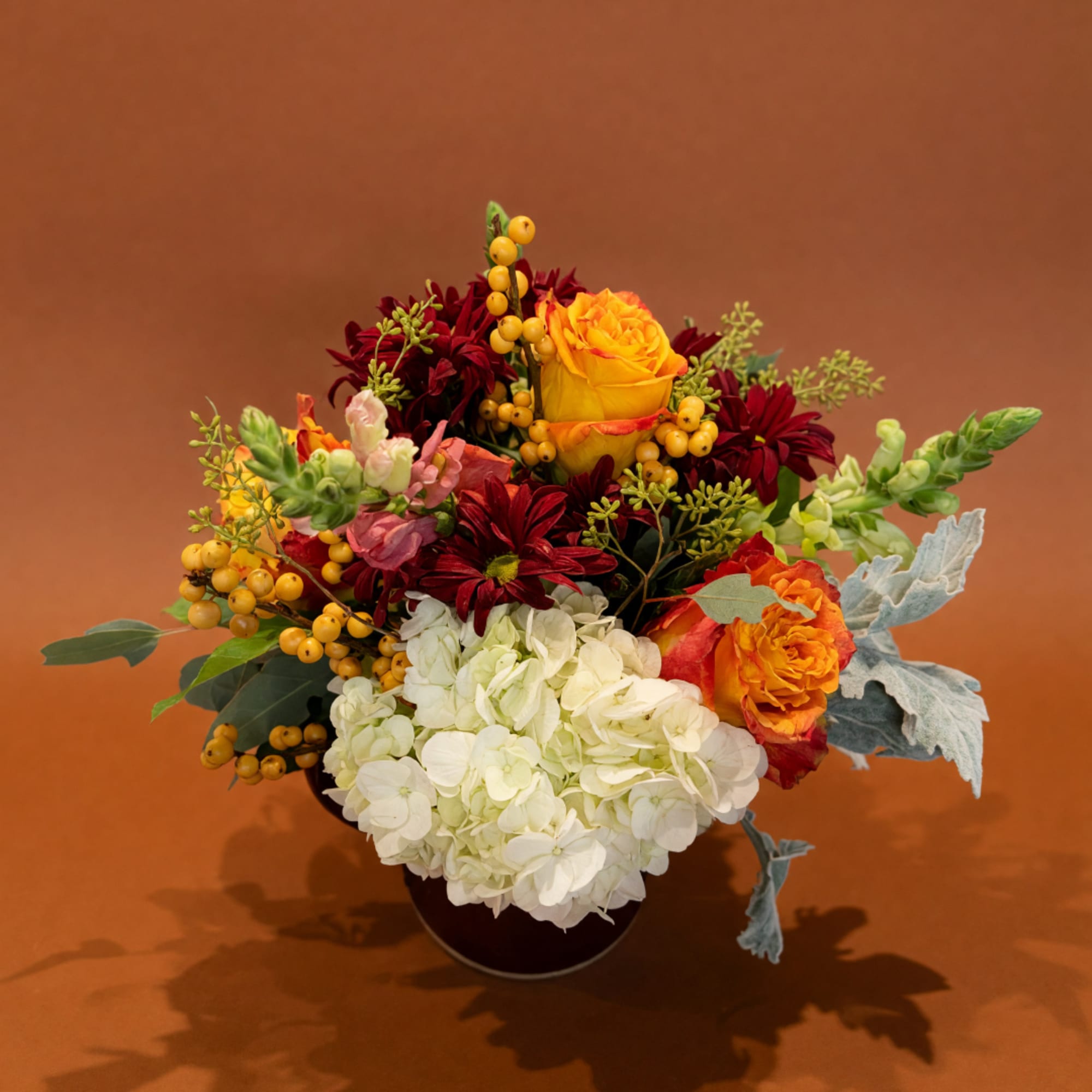 Mixed bouquet with yellow roses, white hydrangea, and burgundy flowers in a dark vase