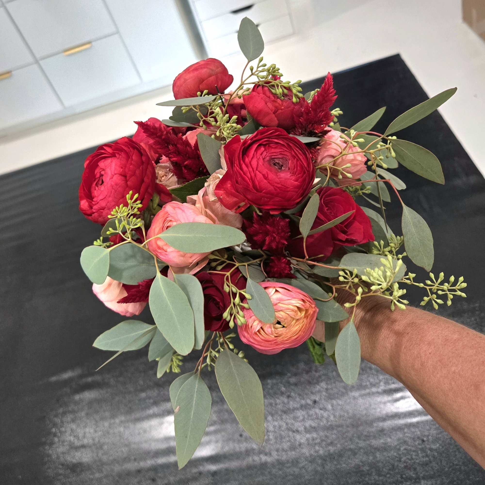 Handheld bouquet of red and pink flowers with eucalyptus foliage