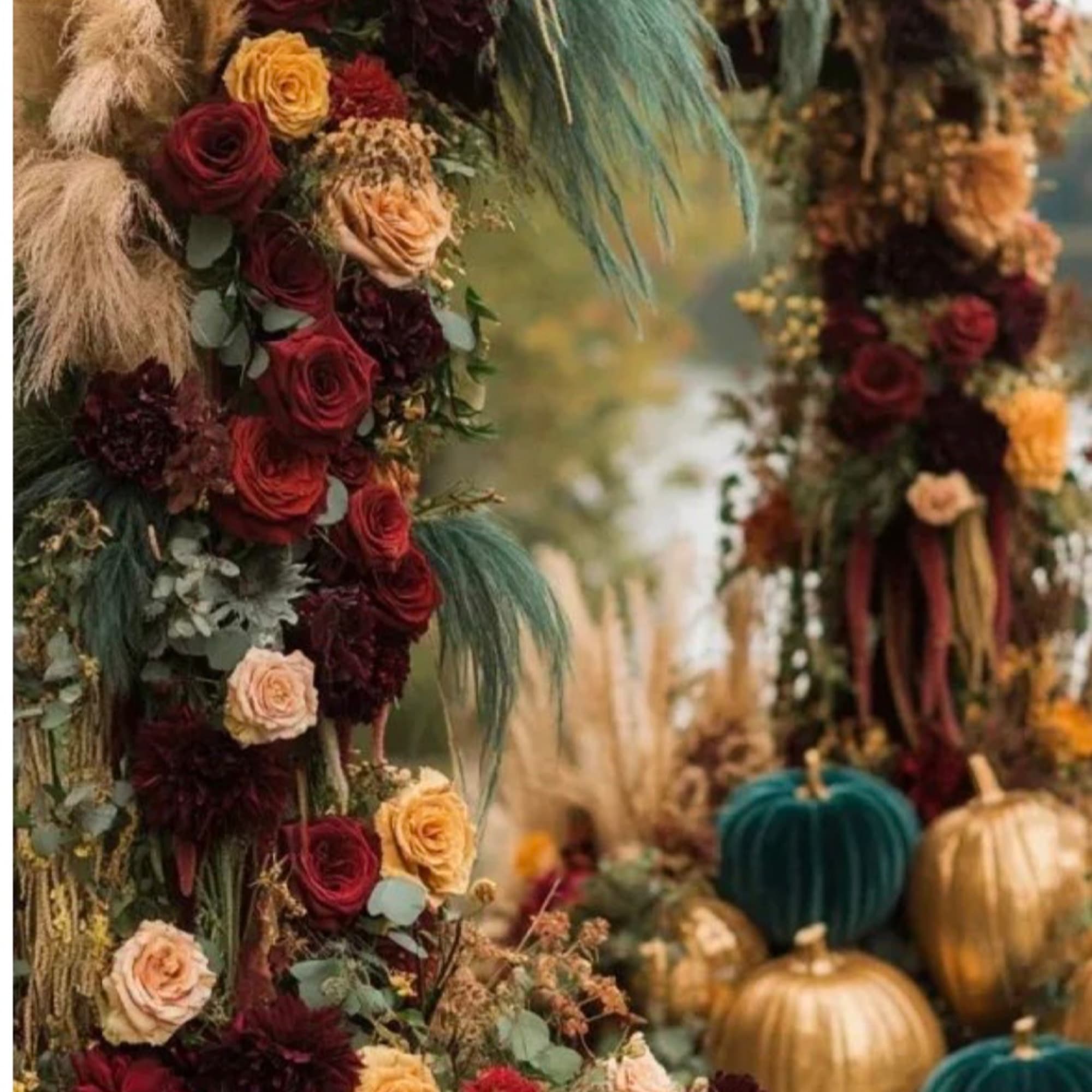 Floral pillar with roses and dried grasses beside decorative pumpkins