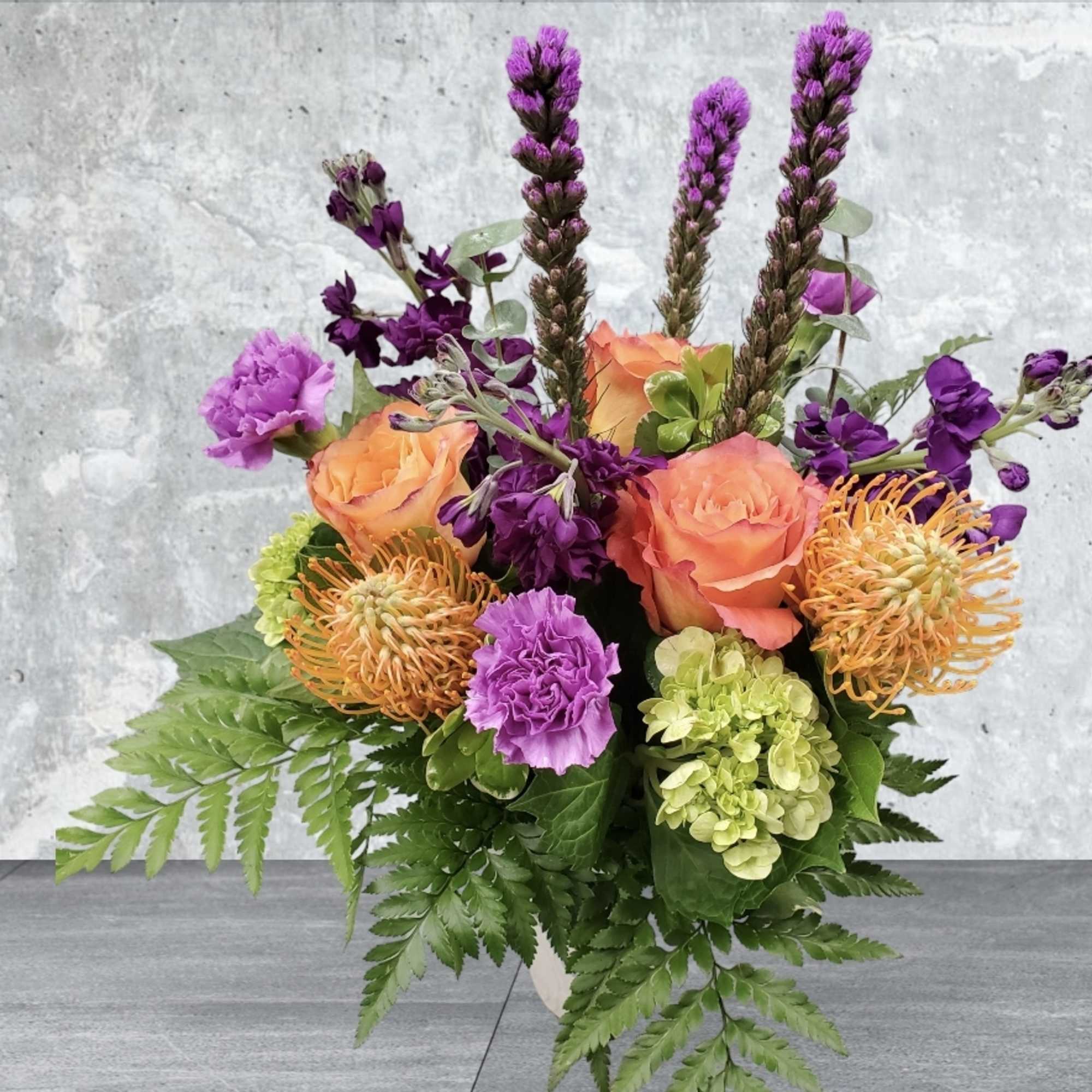 Bouquet with peach roses, purple flowers, and green hydrangeas in a vase