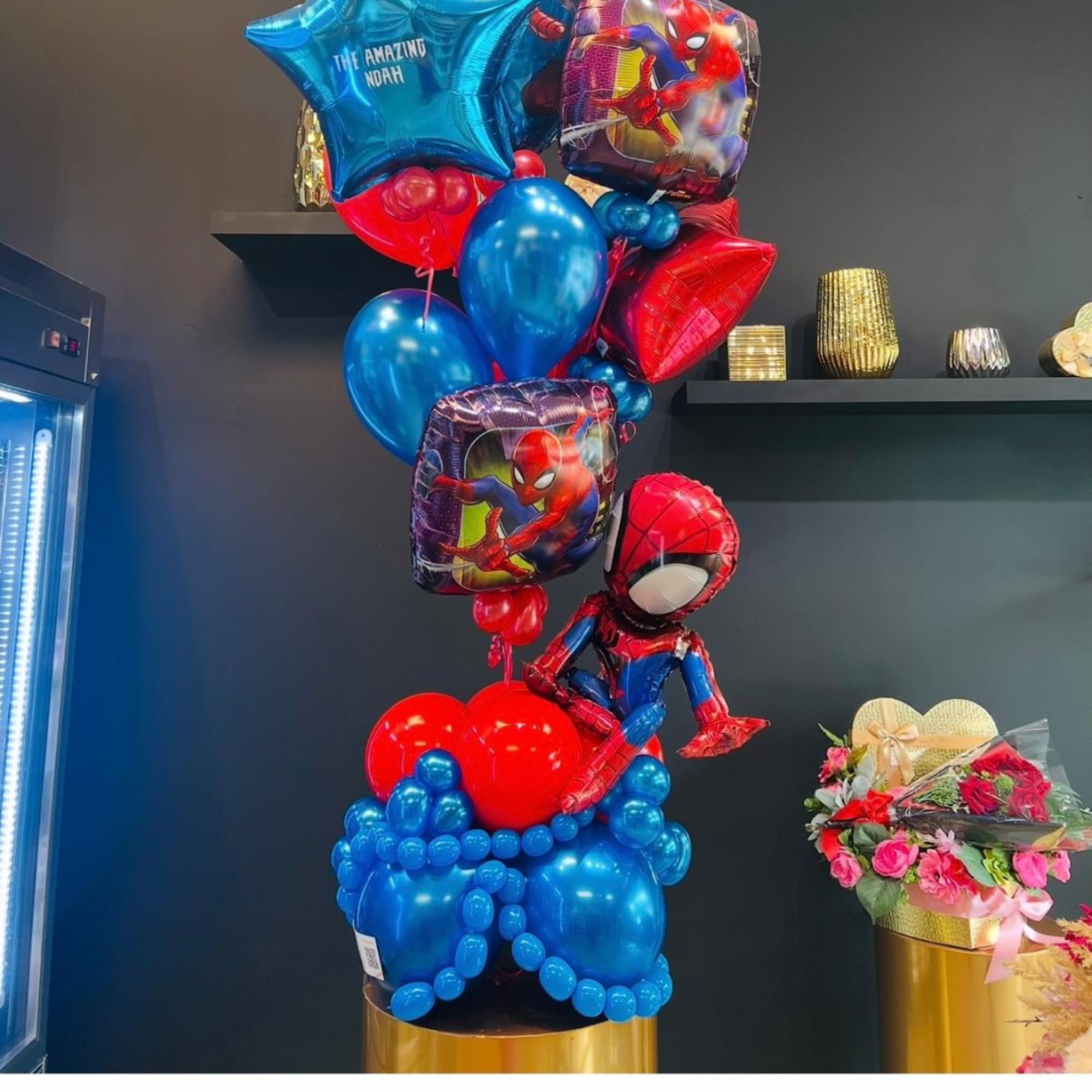 Spider-Man balloons with blue and red balloons beside a small pink rose bouquet