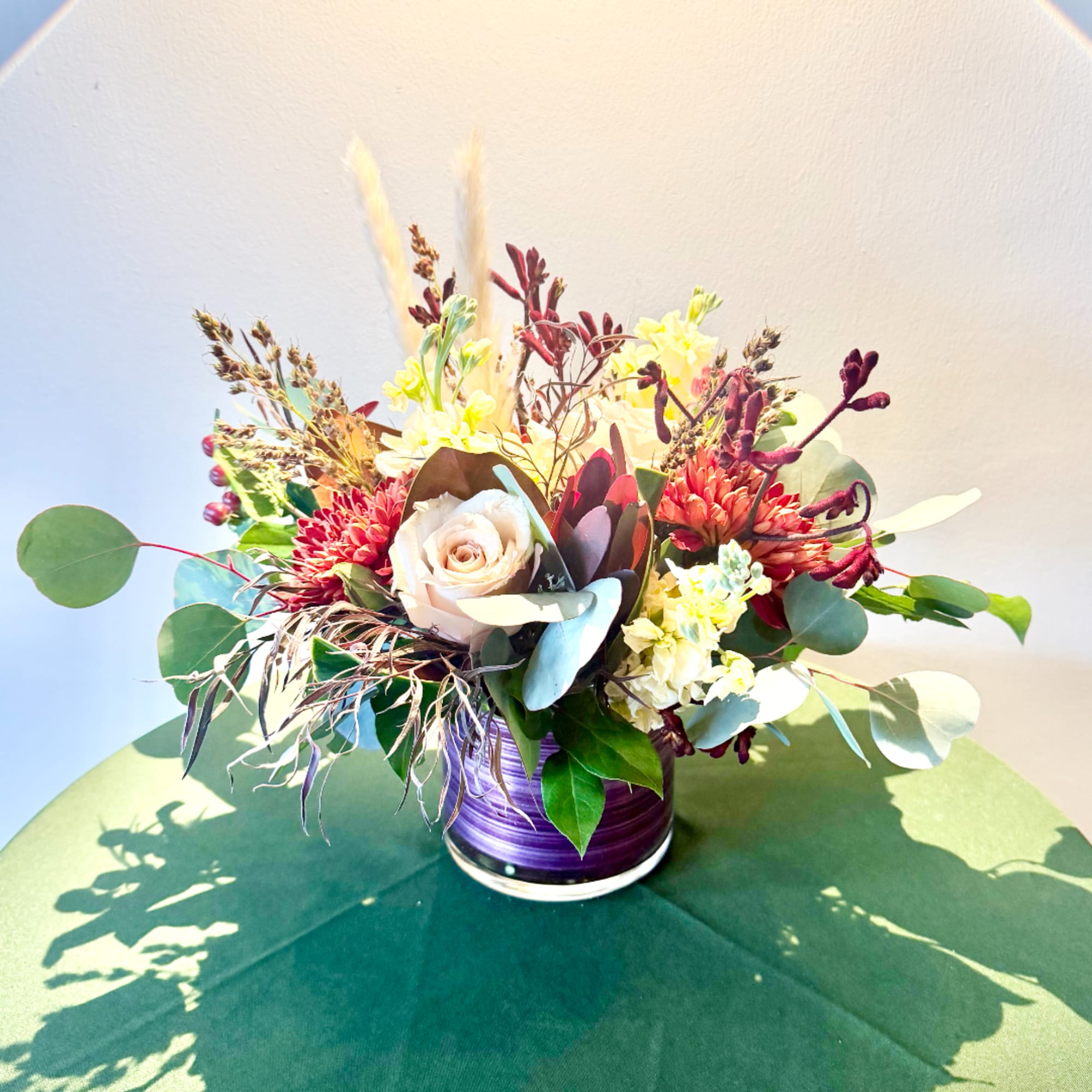 Mixed floral arrangement in a purple vase with cream and red blooms
