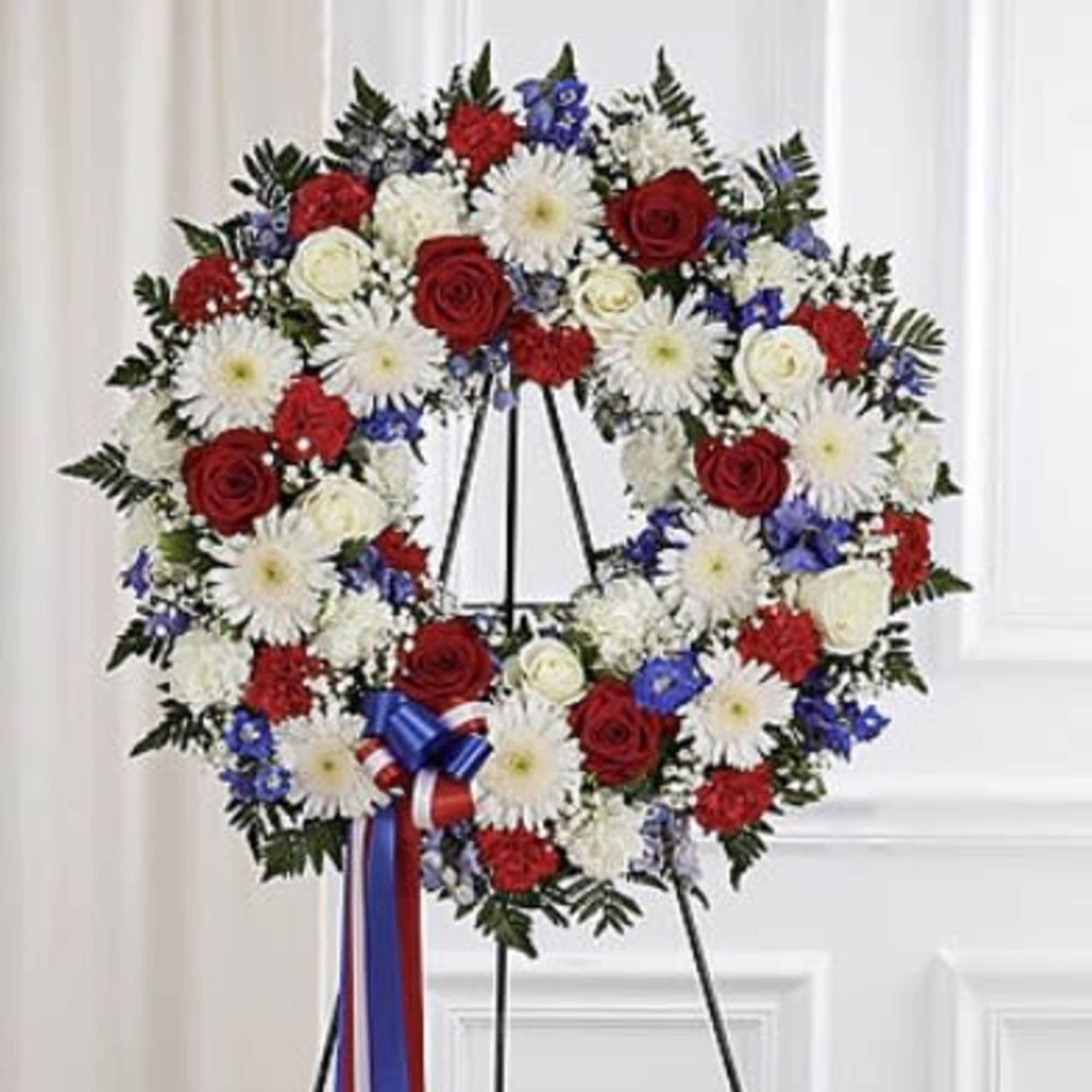 Red, white, and blue floral wreath on a black easel with ribbon