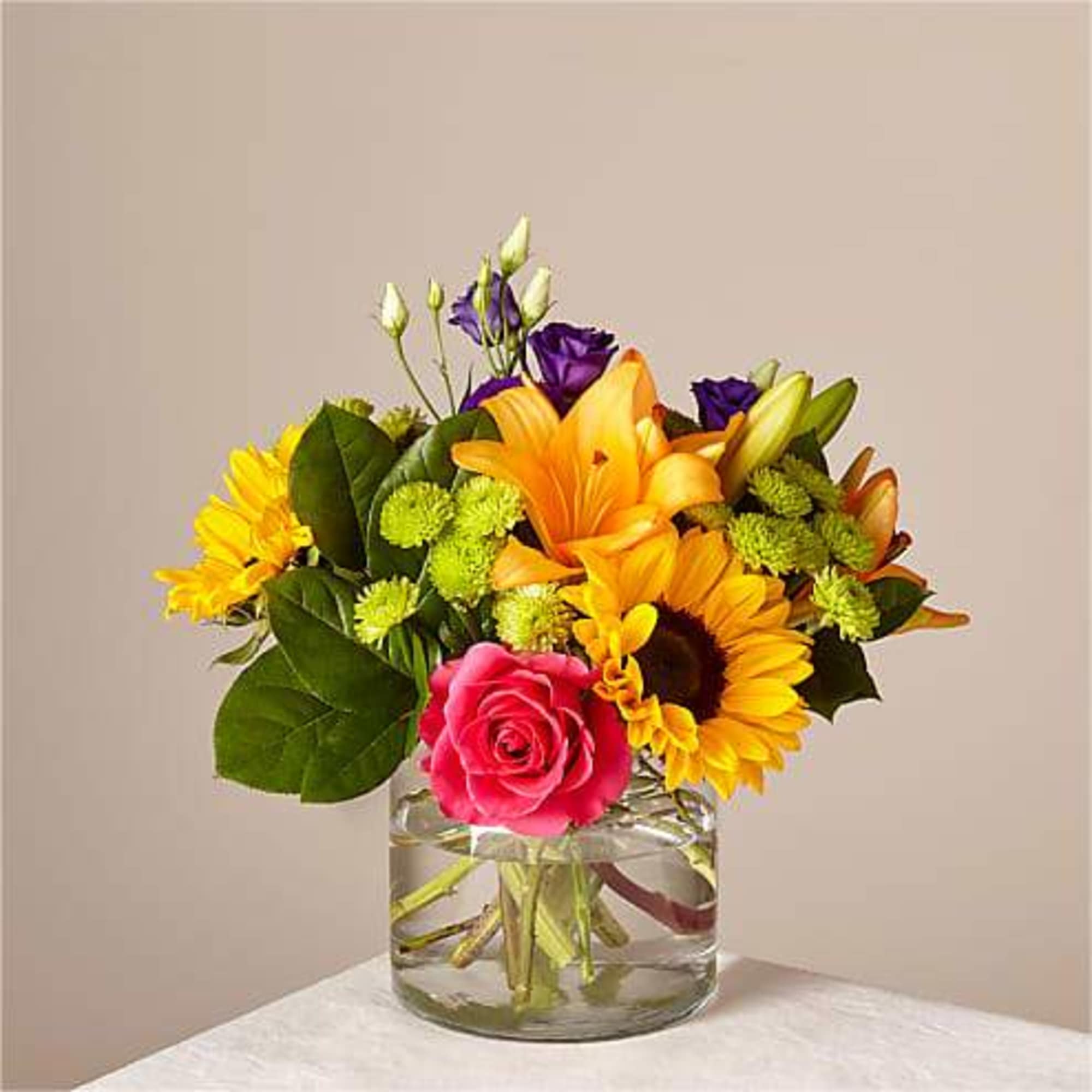 Mixed bouquet of sunflowers, roses, and lilies in a glass vase