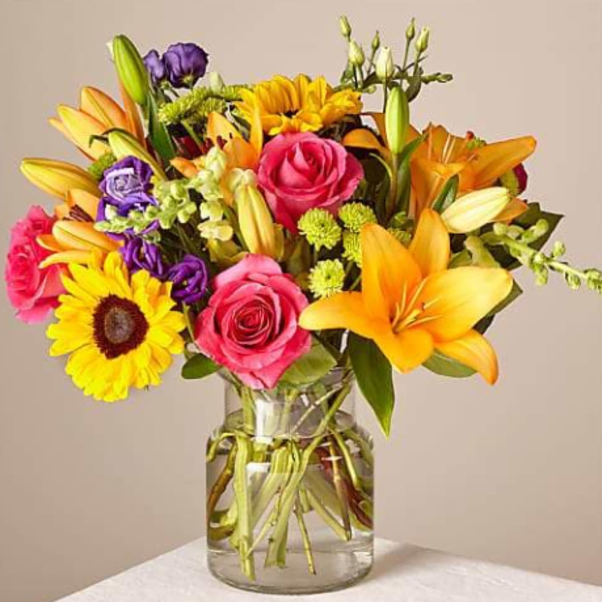 Colorful bouquet of roses, lilies, and a sunflower in a glass vase