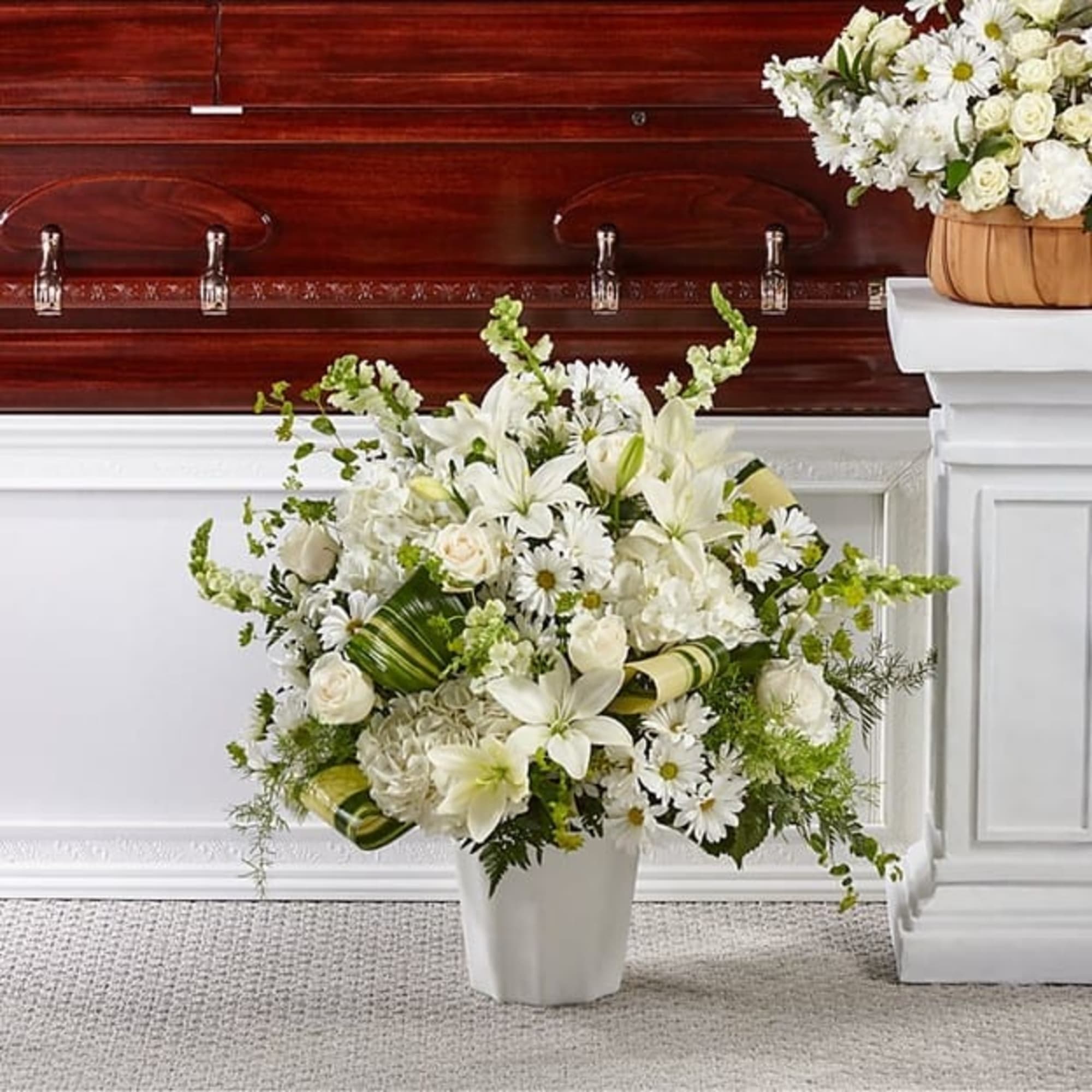 White floral arrangement in a white vase beside a casket