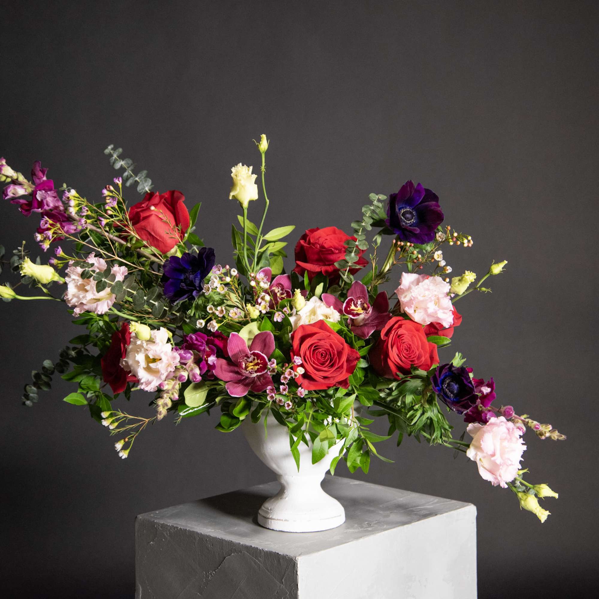 Mixed bouquet of red roses, purple blooms, and pale pink flowers in a white vase