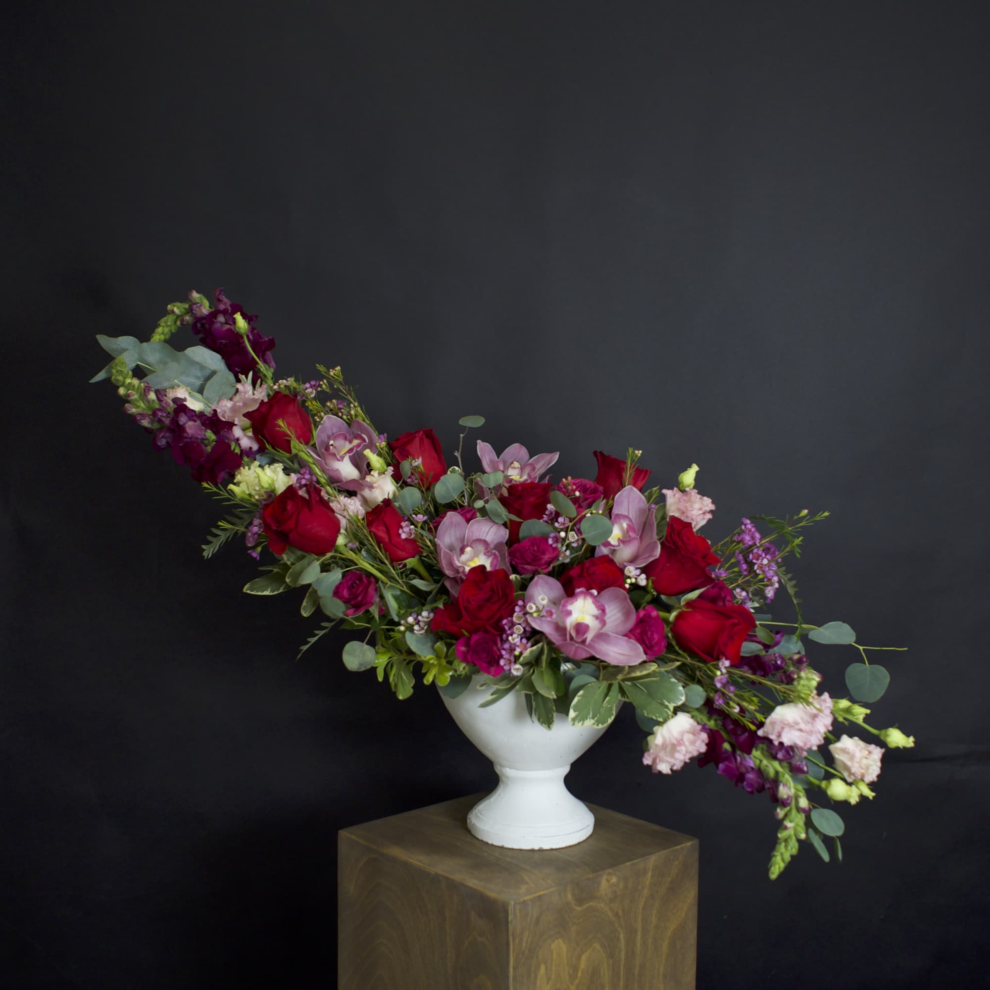 Long floral arrangement of red and pink blooms in a white pedestal vase