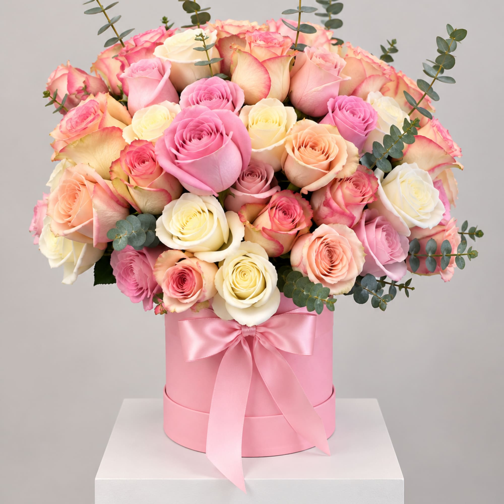 Pink and cream roses arranged in a pink hat box with a ribbon