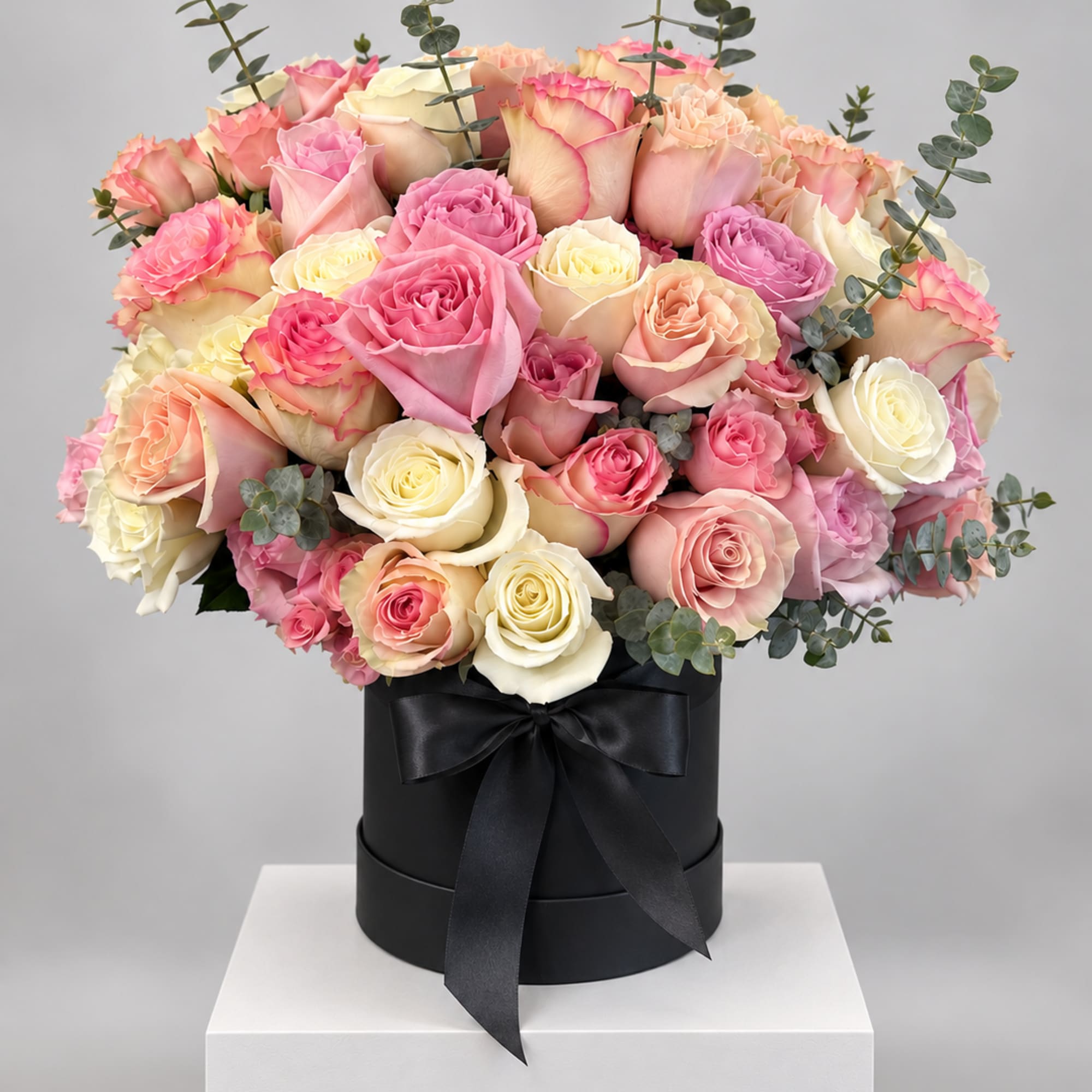 Pink and cream roses arranged in a black hat box with a ribbon