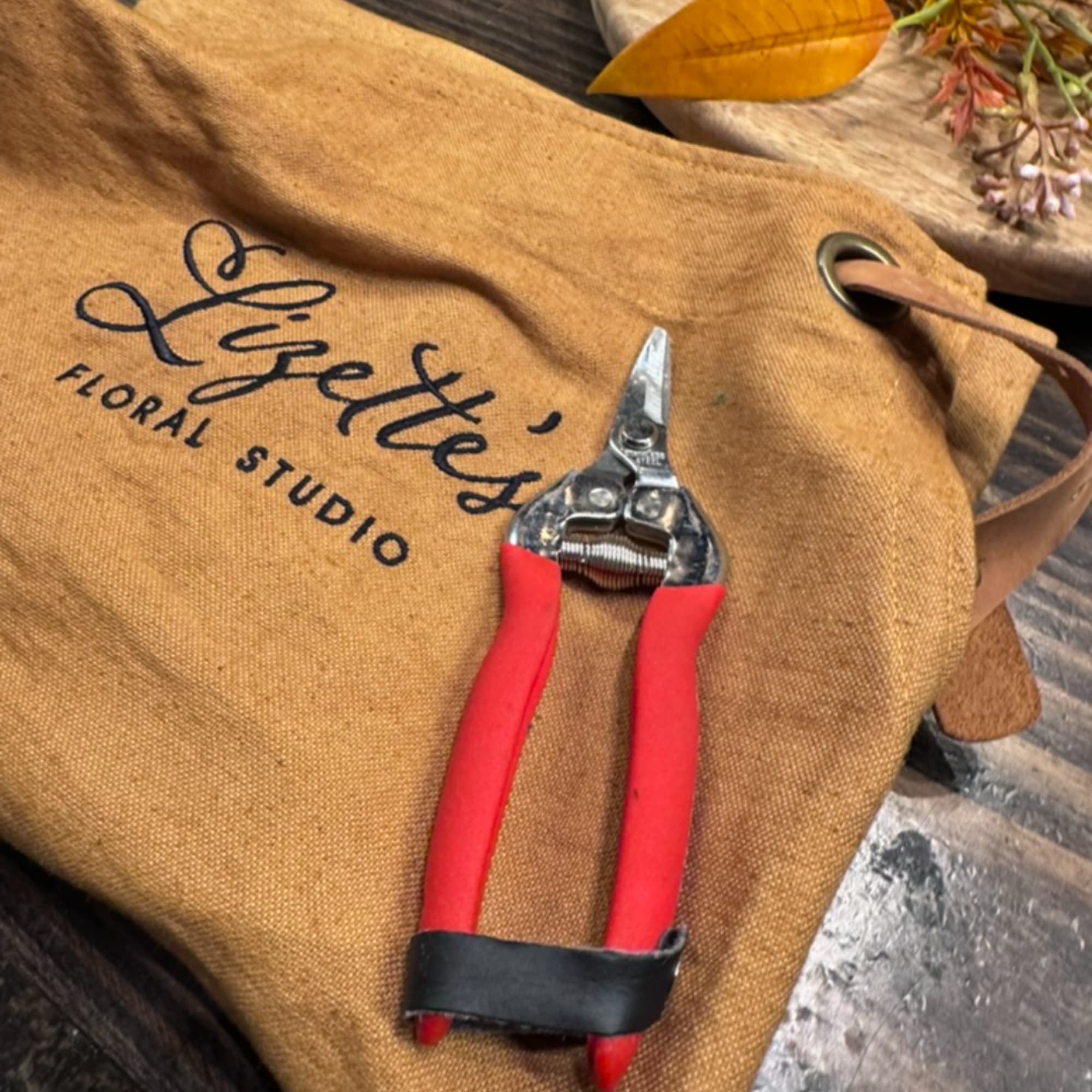 Red-handled pruning shears on a tan floral studio bag