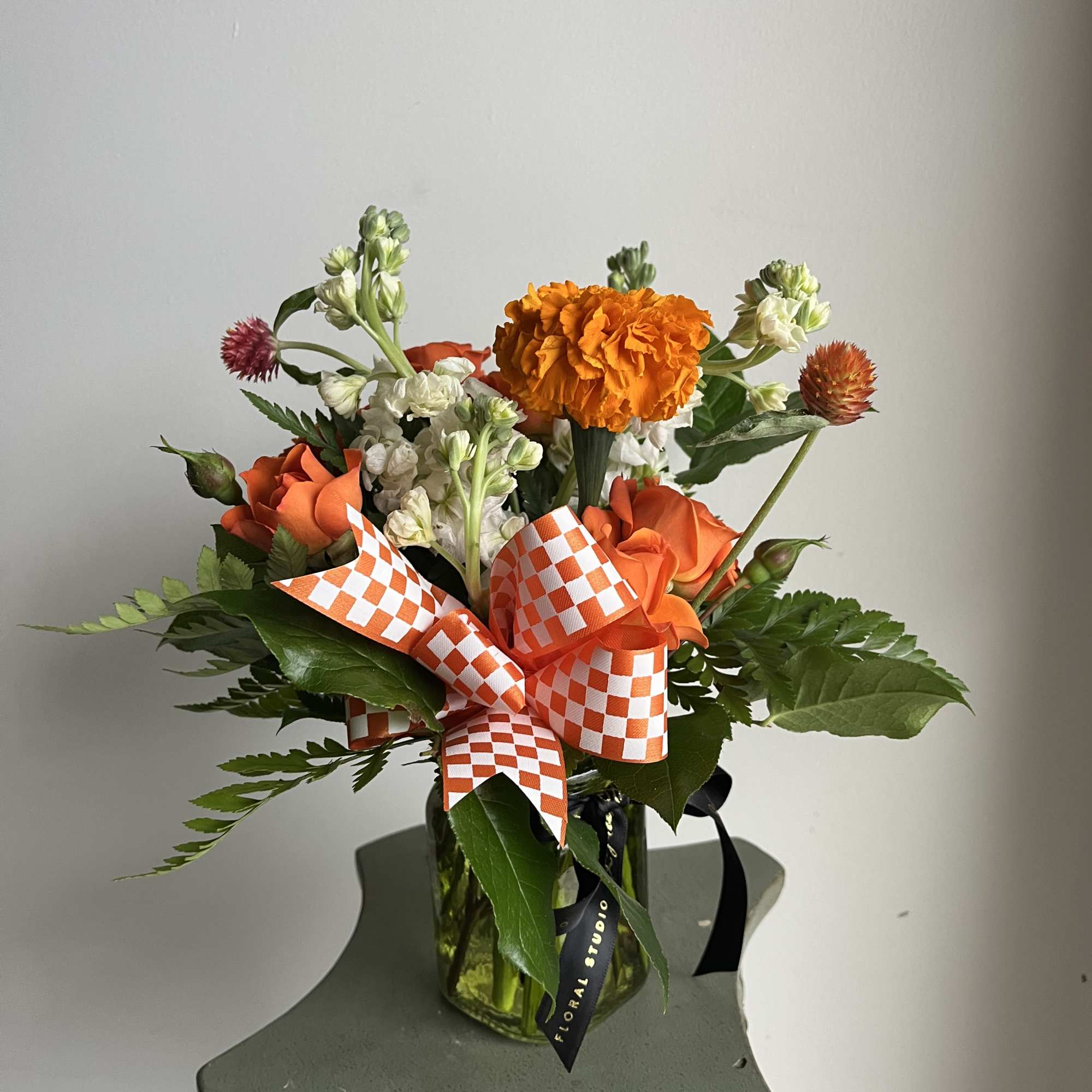 Orange and white mixed bouquet in a glass vase with checkered ribbon