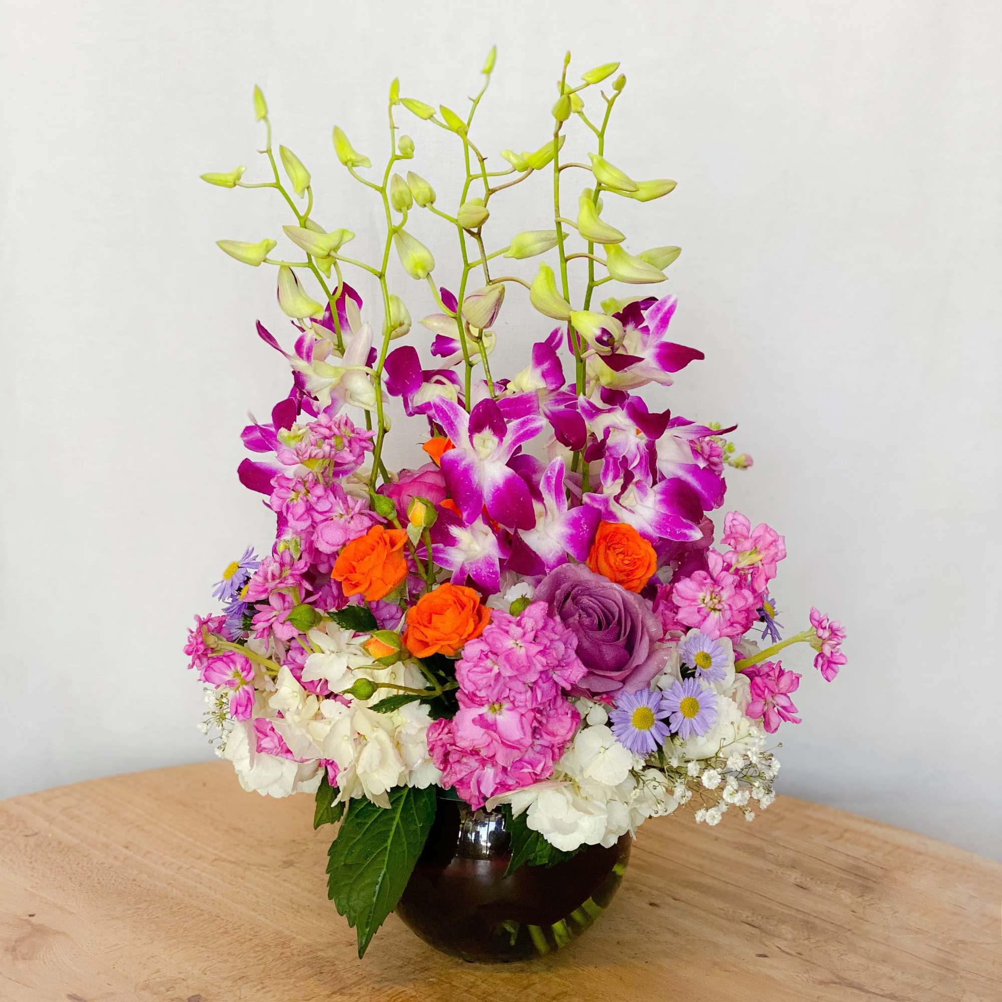 Mixed bouquet with orchids, roses, and carnations in a dark glass vase