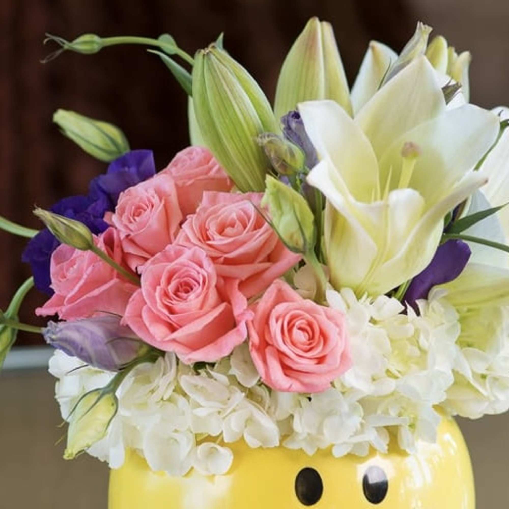 Pink roses and white lilies arranged in a yellow smiley-face vase