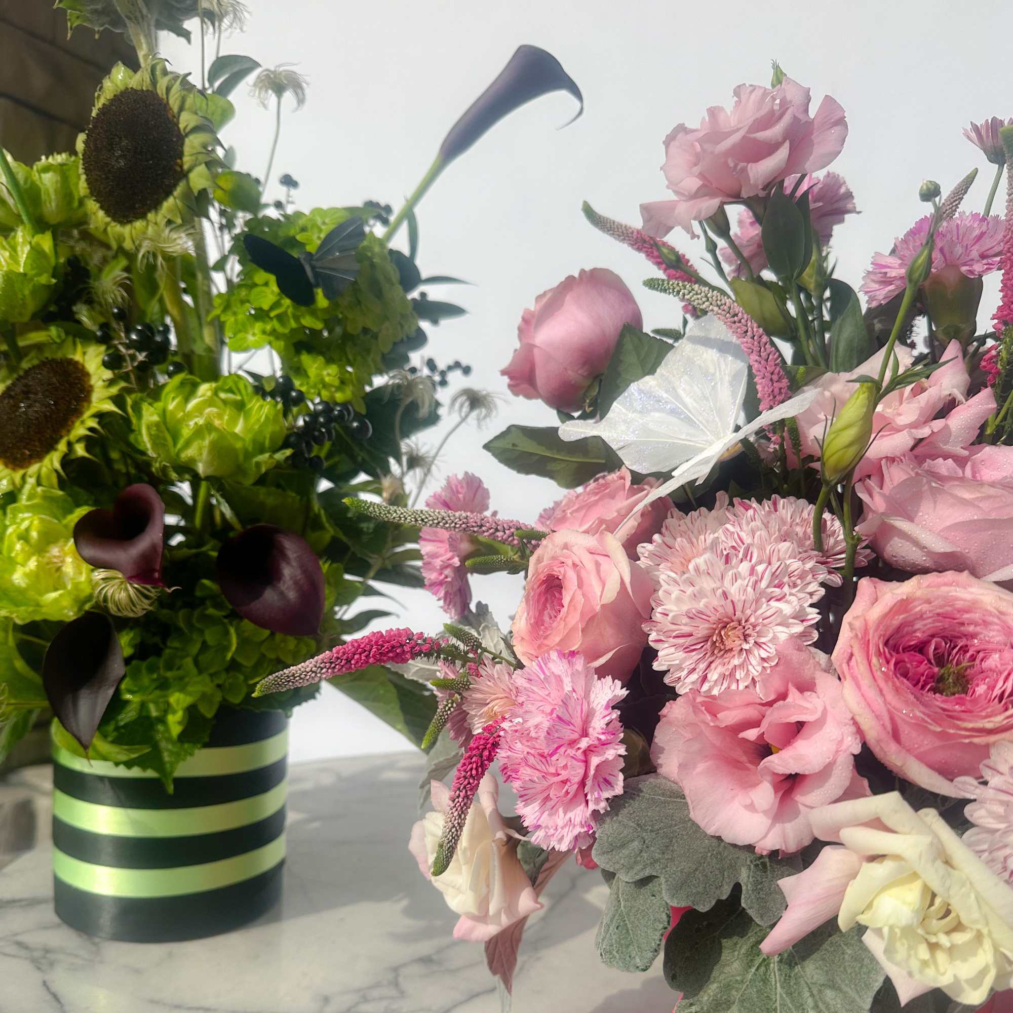 Two floral arrangements, one pink and one green, in striped containers
