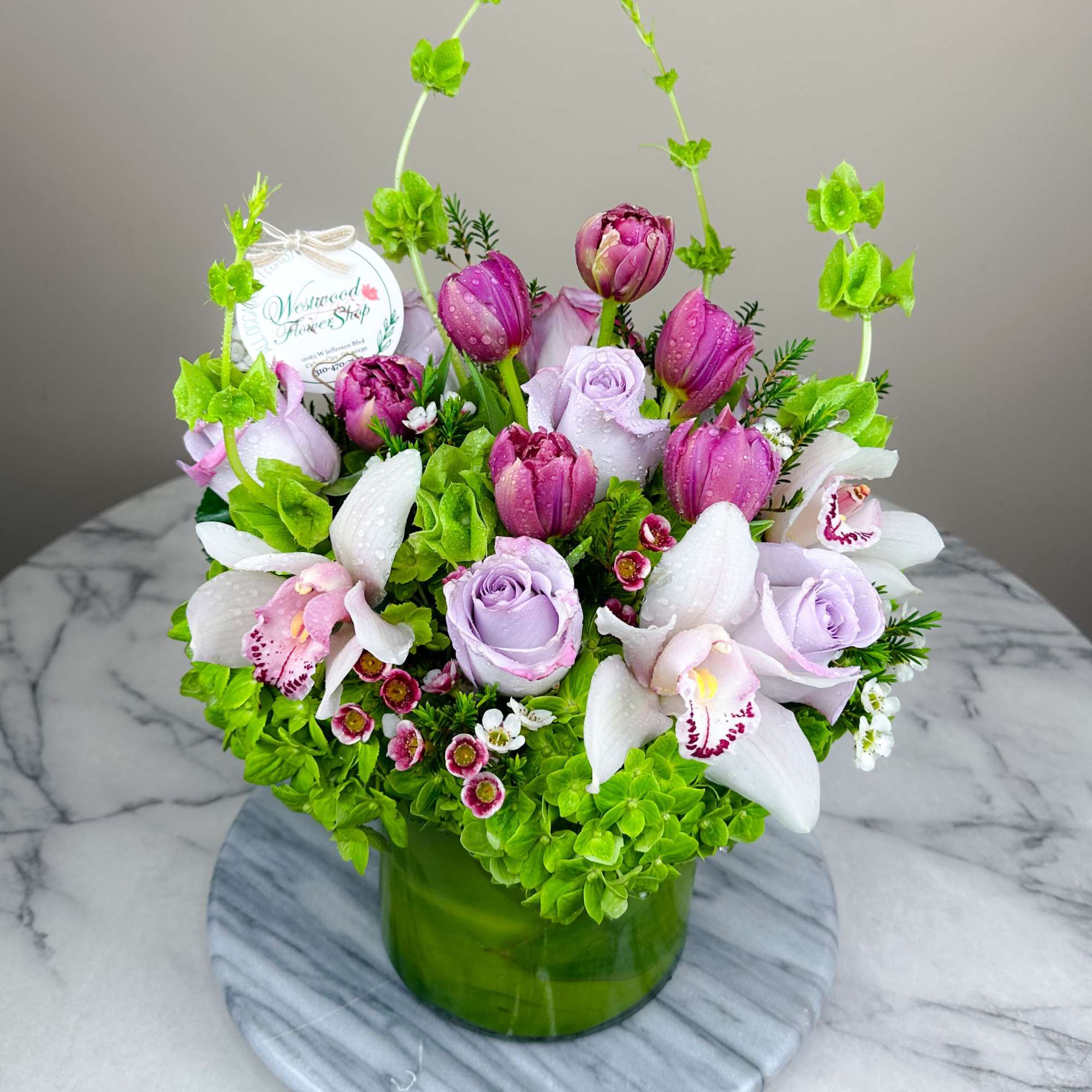 Lavender roses, pink tulips, and white orchids in a green vase