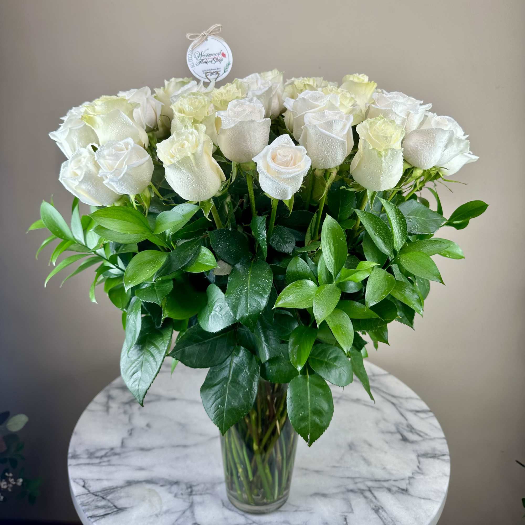 White roses arranged in a clear glass vase with lush green foliage