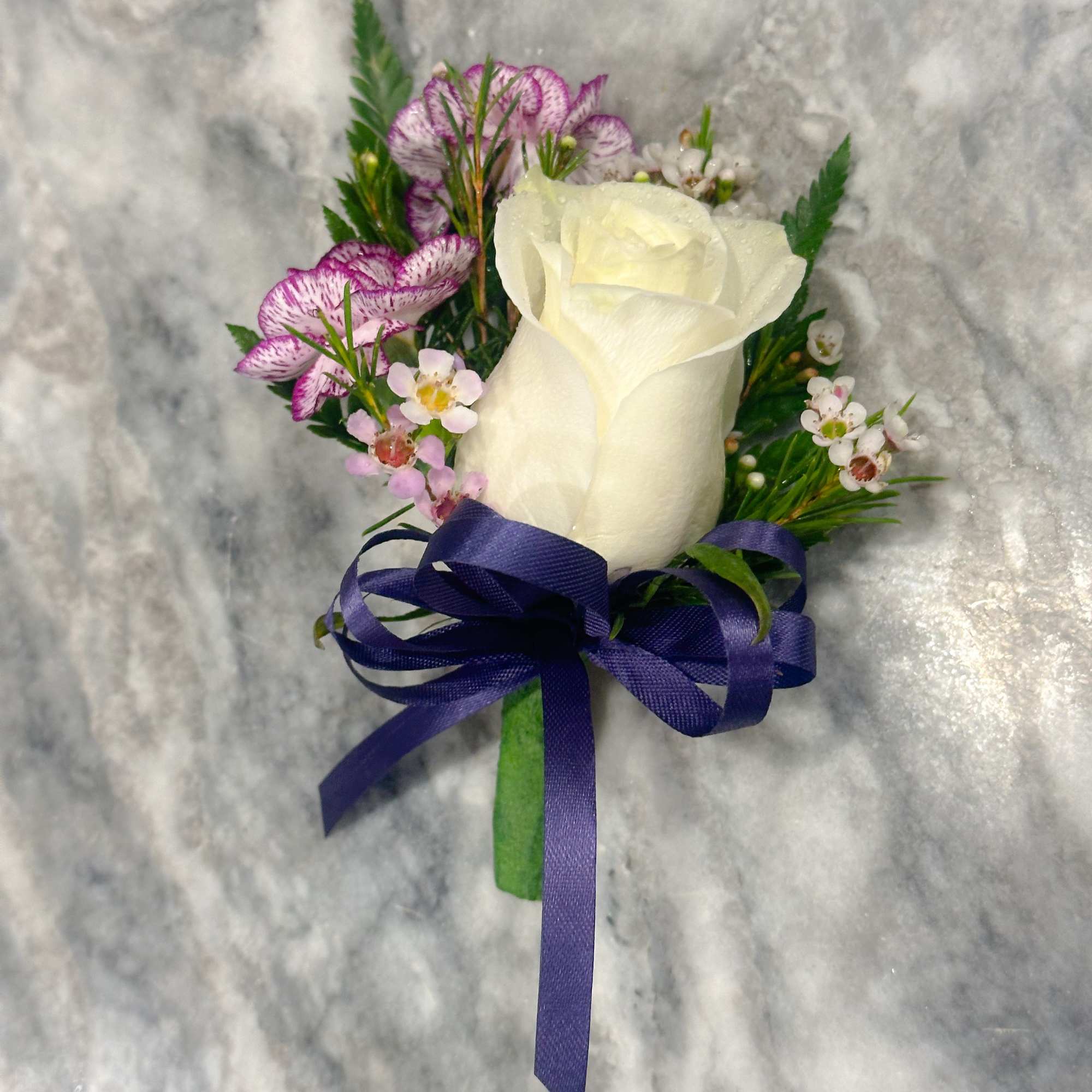 White rose boutonniere with purple flowers and a blue ribbon
