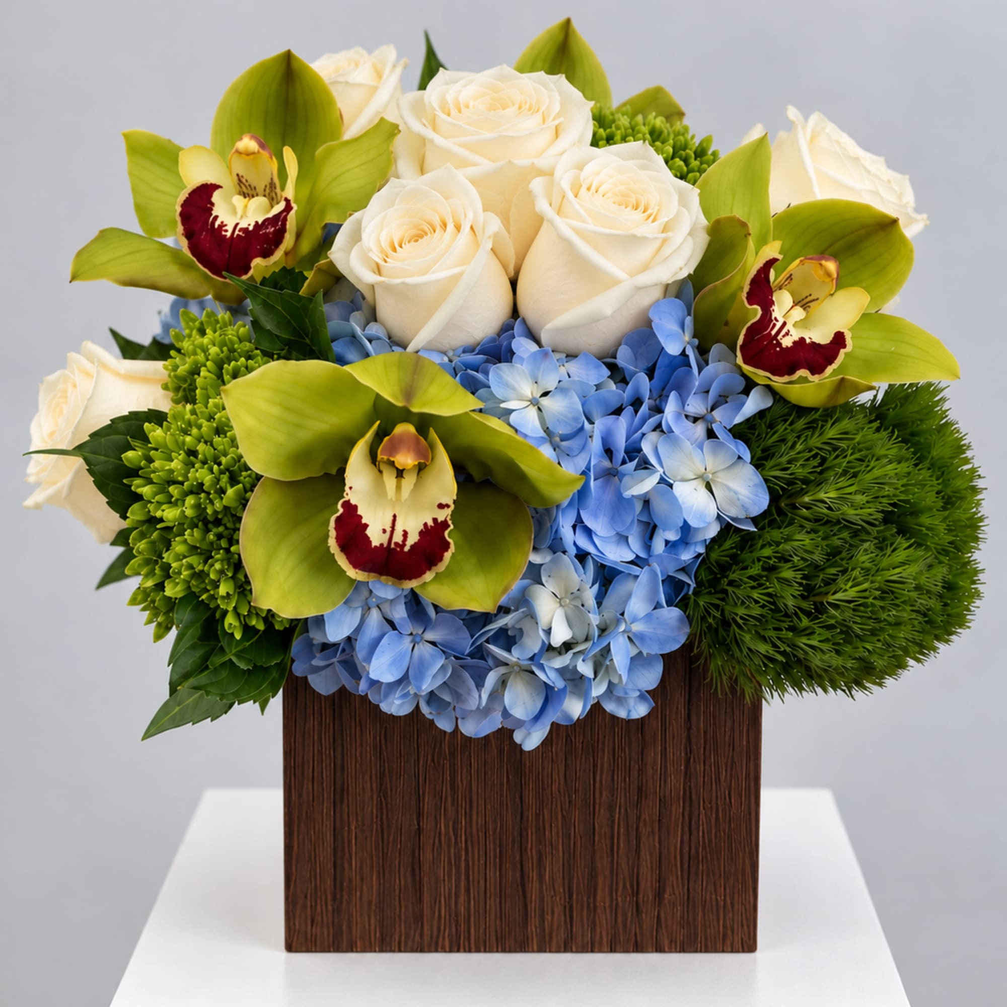 White roses, blue hydrangeas, and green orchids in a square wooden vase