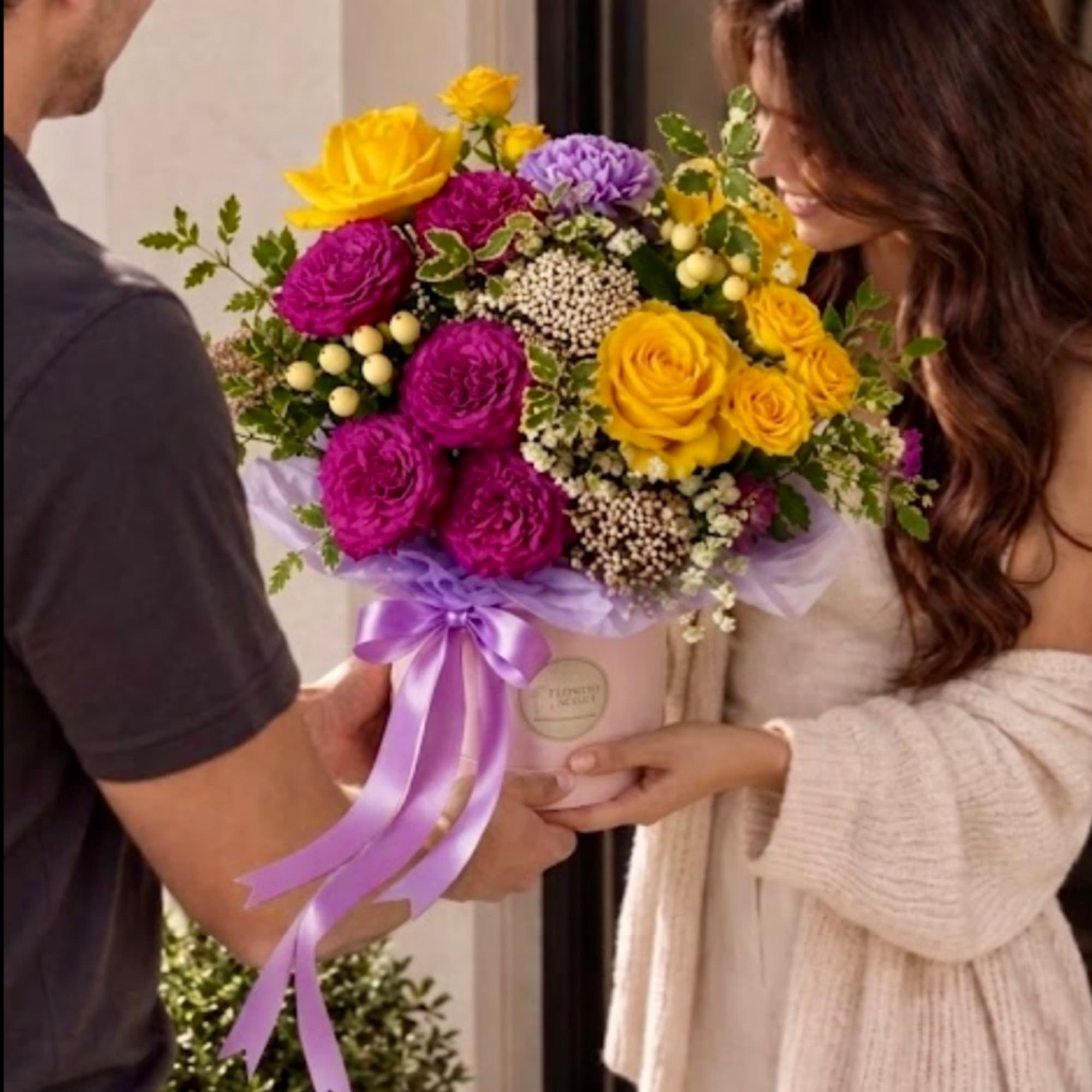 Bright mixed bouquet in a round box with a purple ribbon
