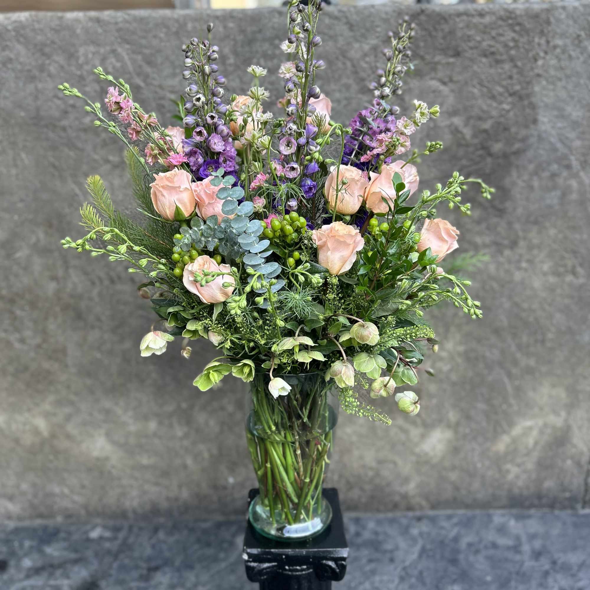 Tall bouquet of blush roses and purple flowers in a glass vase
