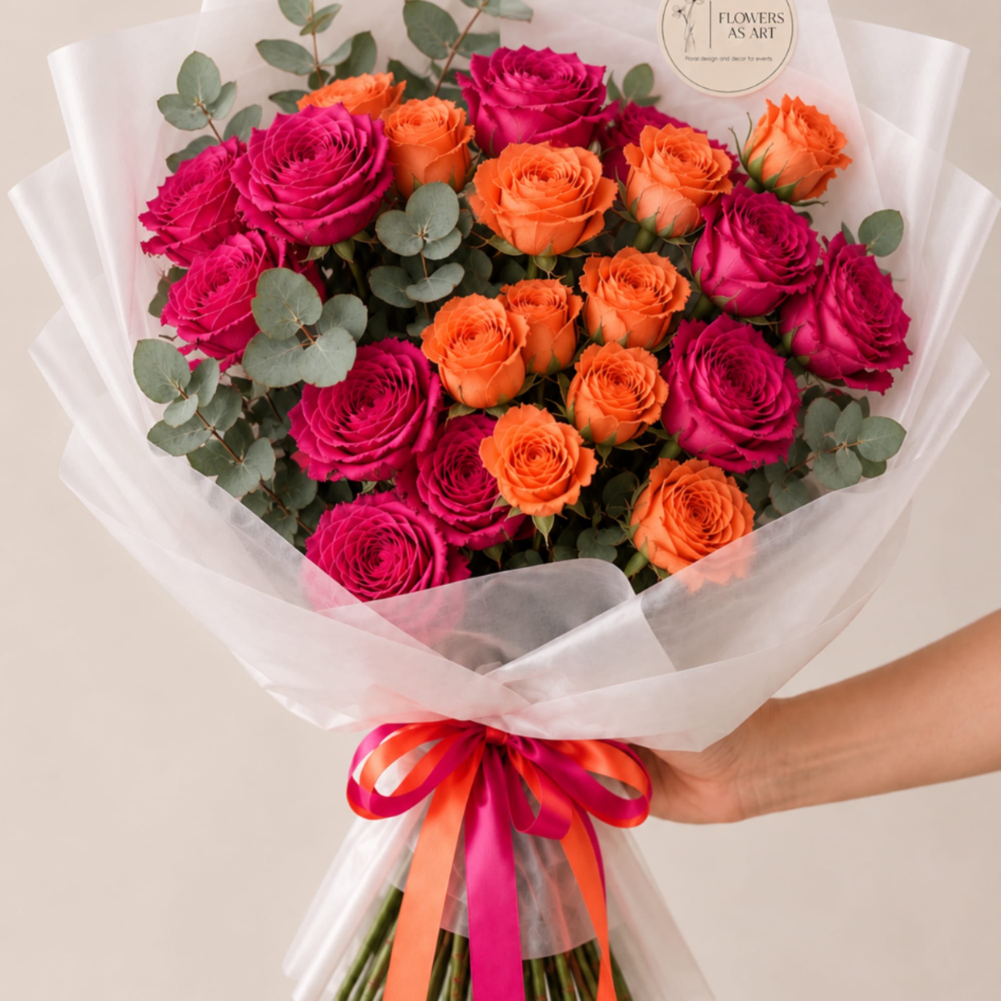 Bouquet of hot pink and orange roses wrapped in white paper with a ribbon