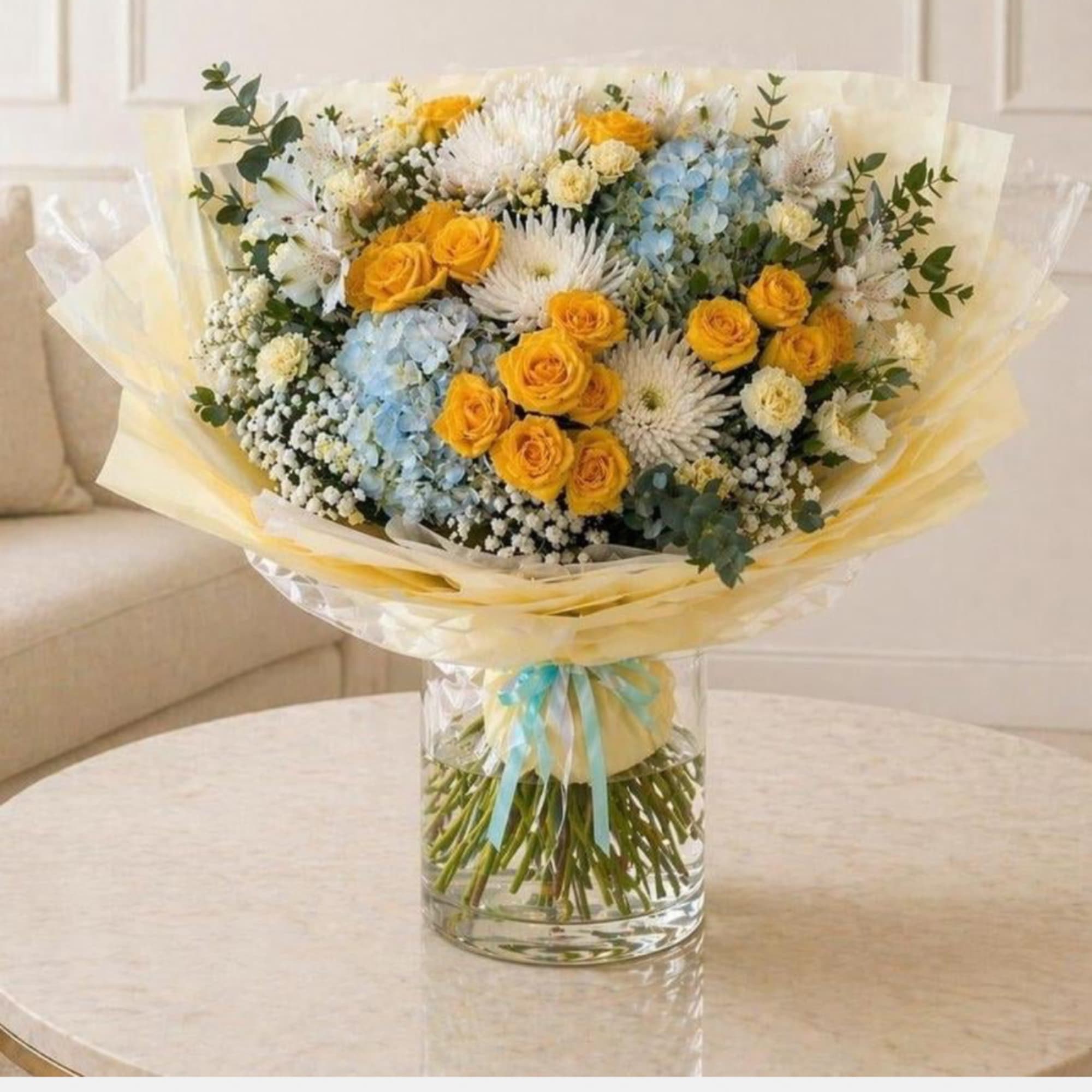 Bouquet of yellow roses, blue hydrangeas, and white flowers in a glass vase