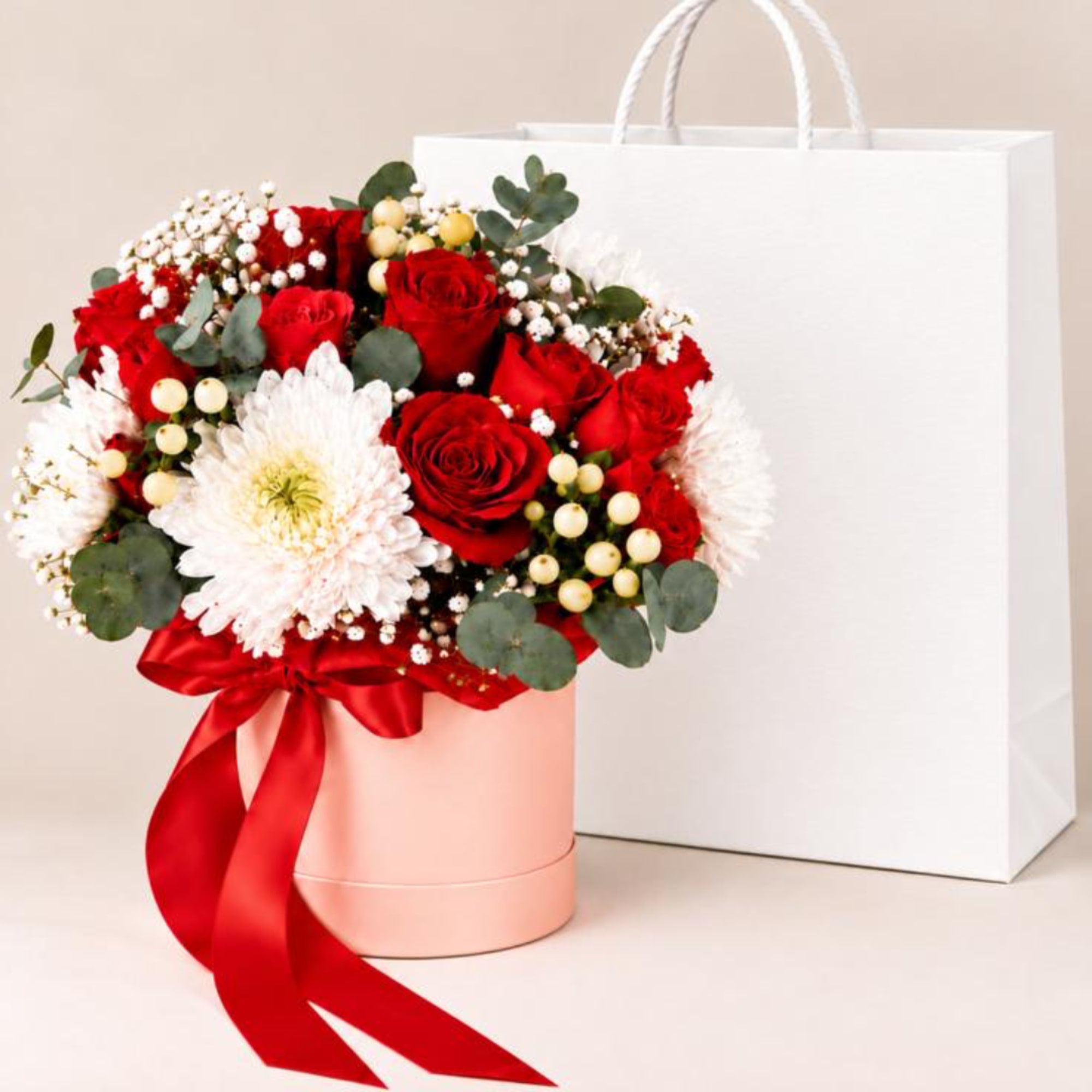 Red roses and white daisies in a pink hat box with a red ribbon
