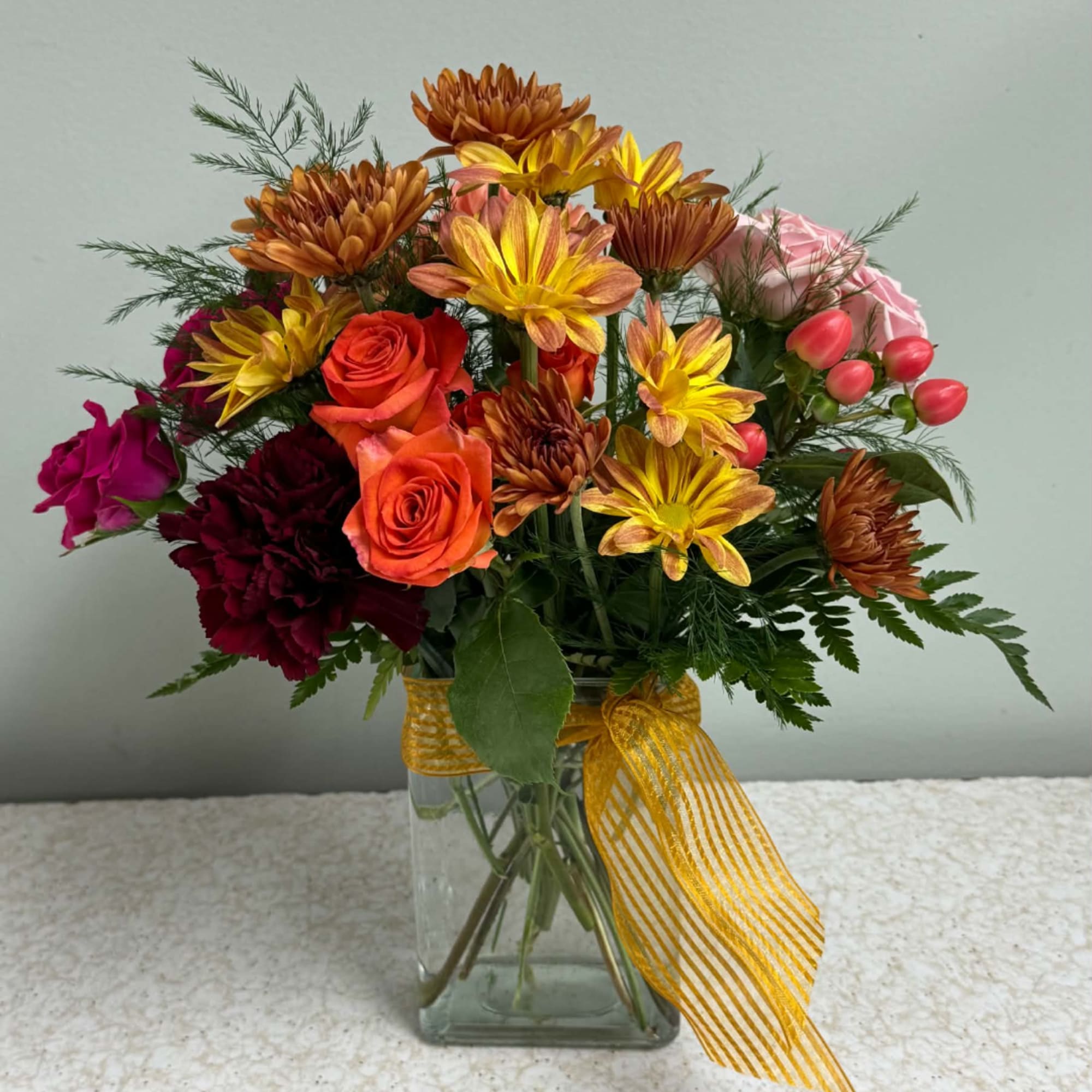 Mixed bouquet of roses and chrysanthemums in a glass vase with a yellow ribbon