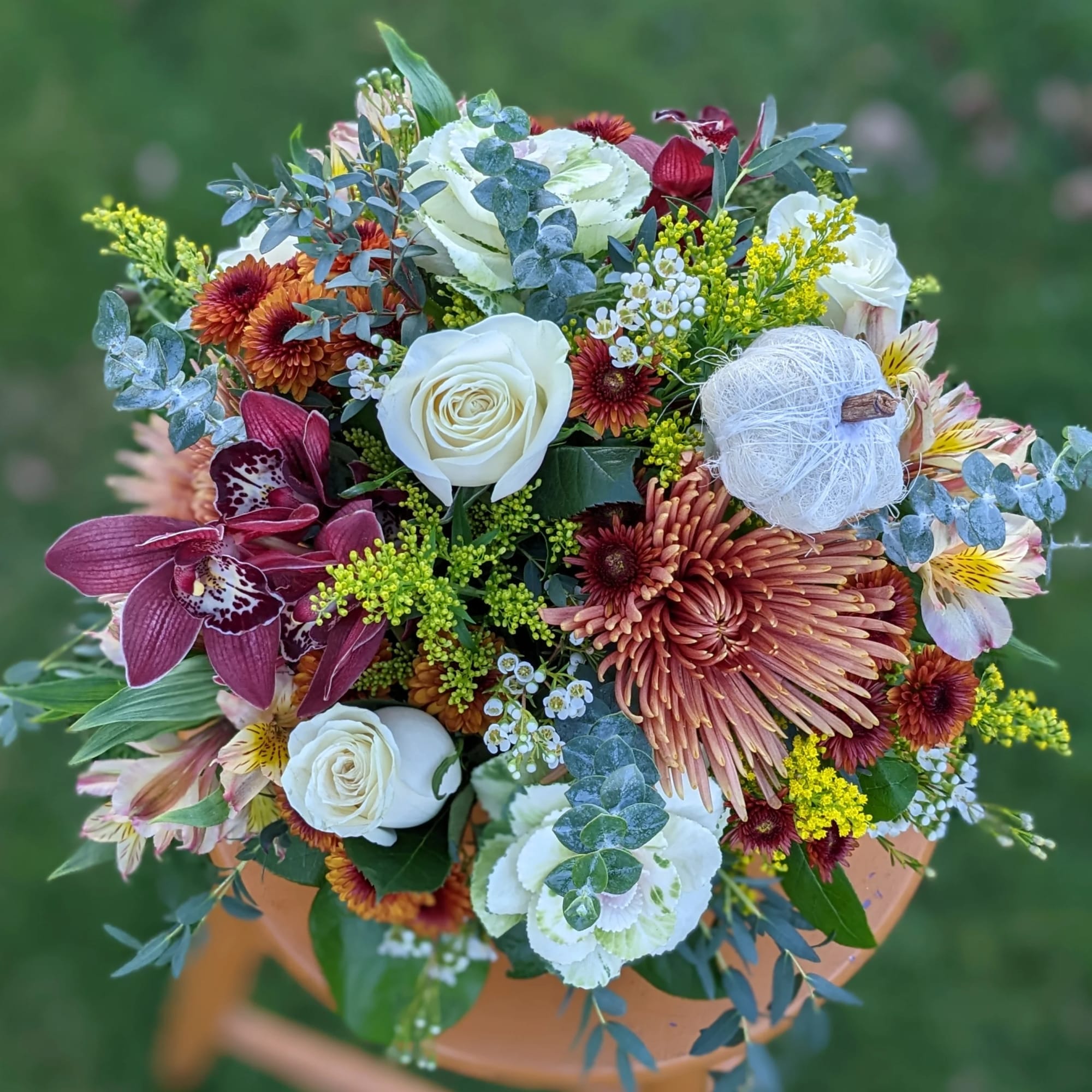 Mixed bouquet with white roses, burgundy orchids, and orange chrysanthemums in a vase