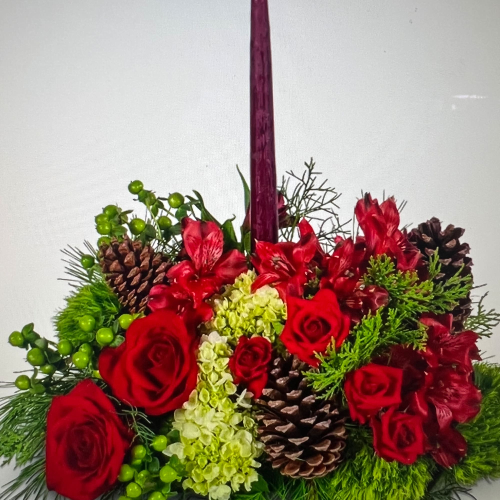Red roses and red lilies arranged with pinecones in a tall vase.