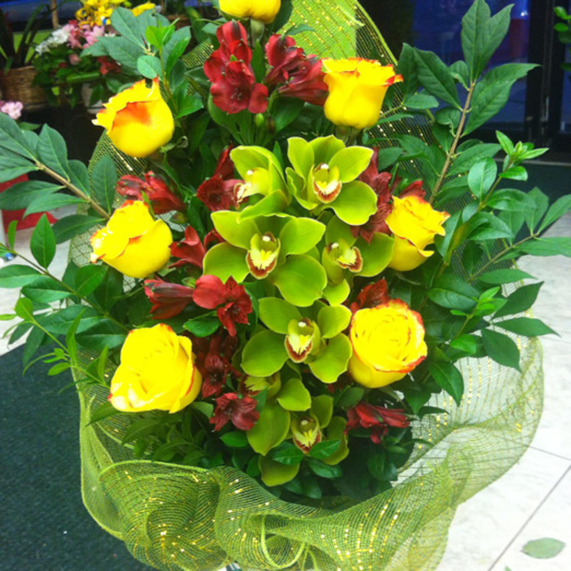Bouquet of yellow roses, green orchids, and red flowers in a white vase
