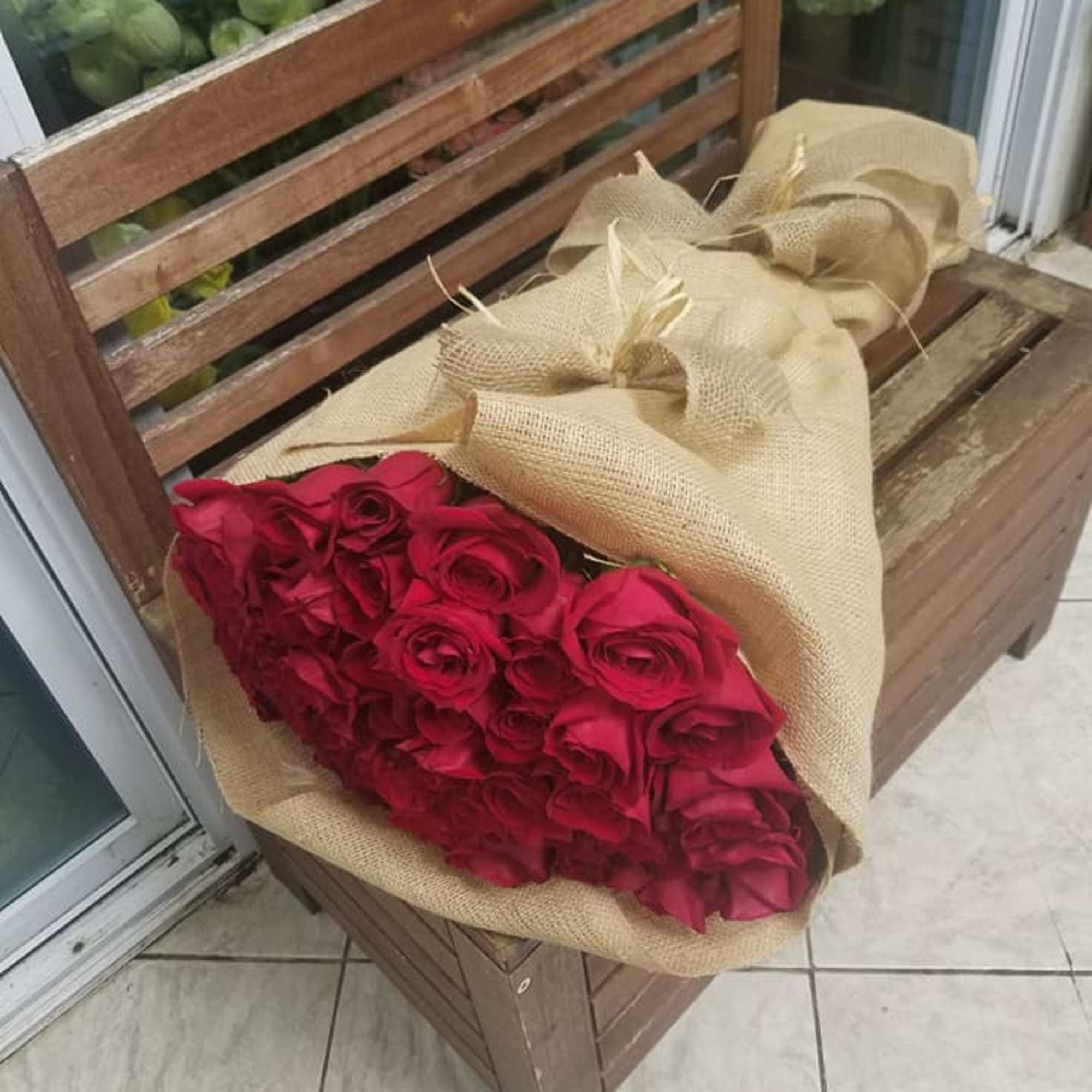 Bouquet of red roses wrapped in burlap on a wooden bench