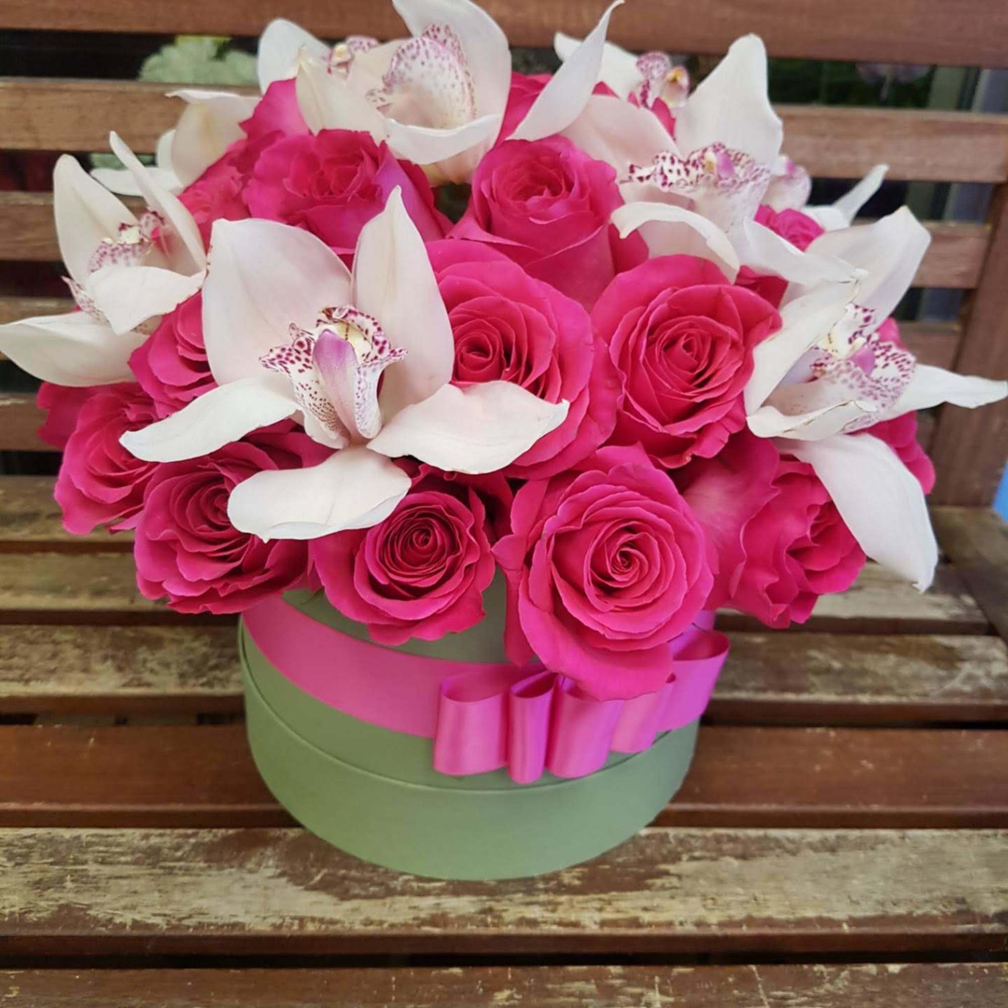 Pink roses and white orchids arranged in a round box with a ribbon.