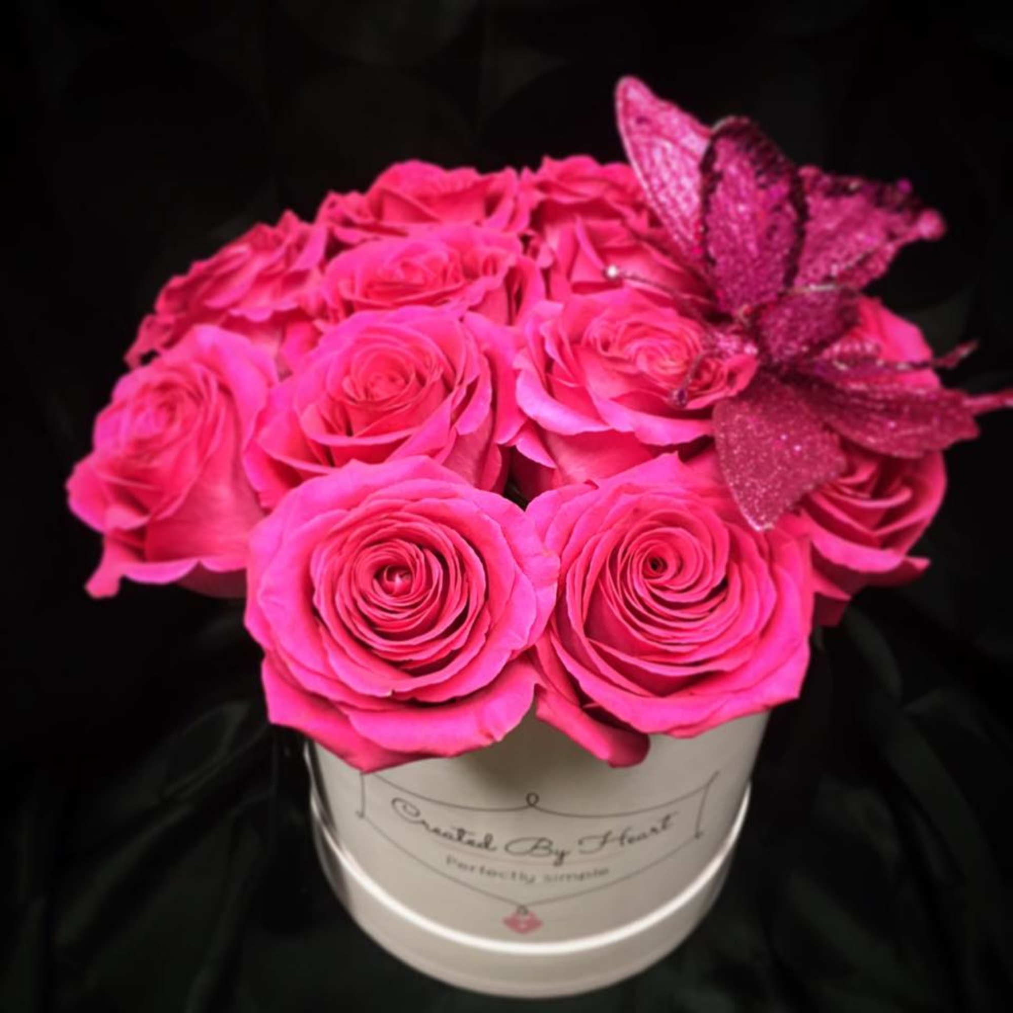 Hot pink roses arranged in a white hat box with a glittery butterfly accent