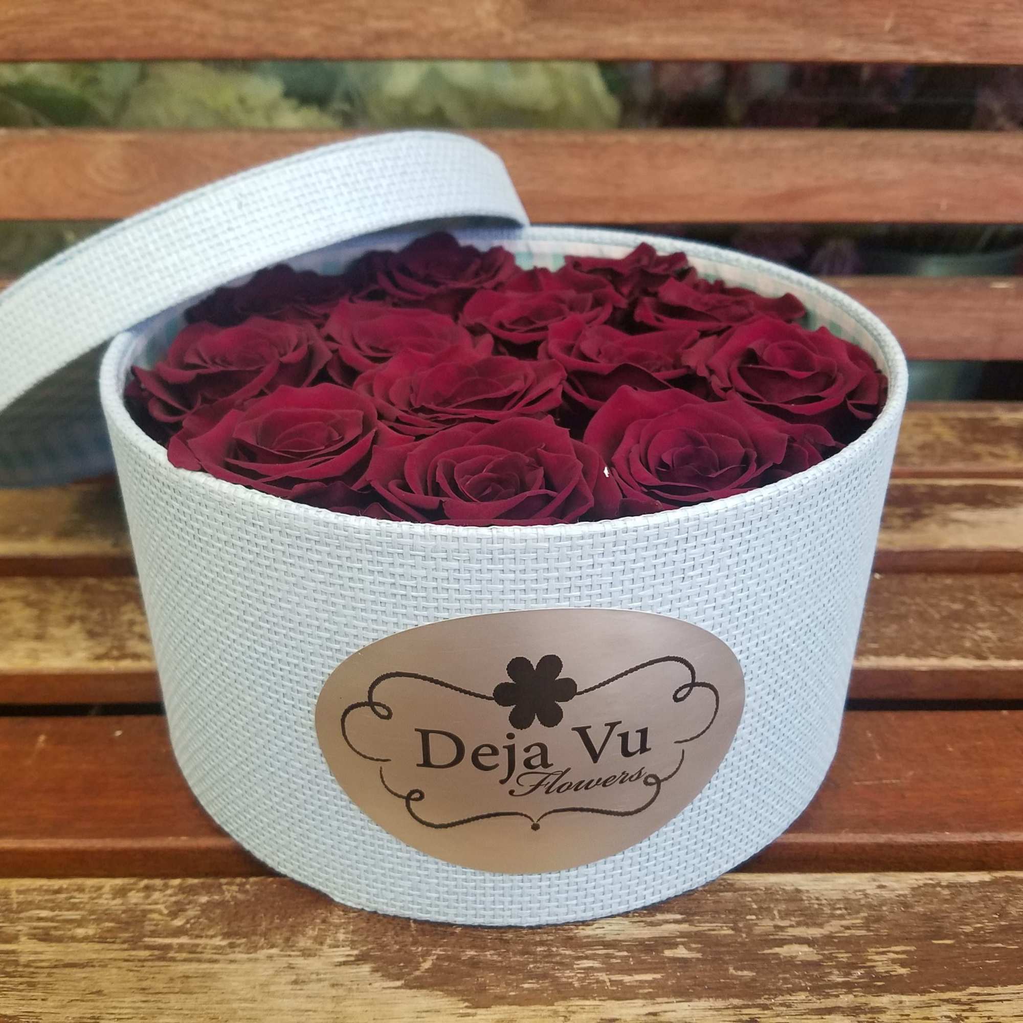 Round white box filled with deep red roses and a lid leaning open