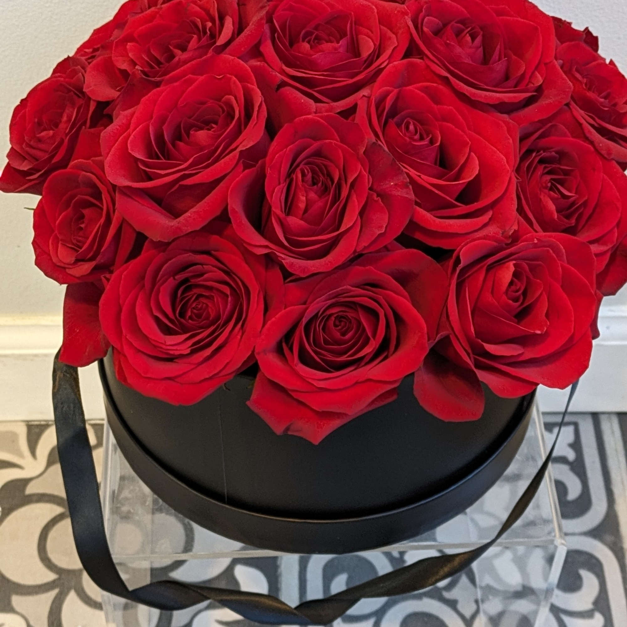 A round black box filled with red roses and tied with a black ribbon.