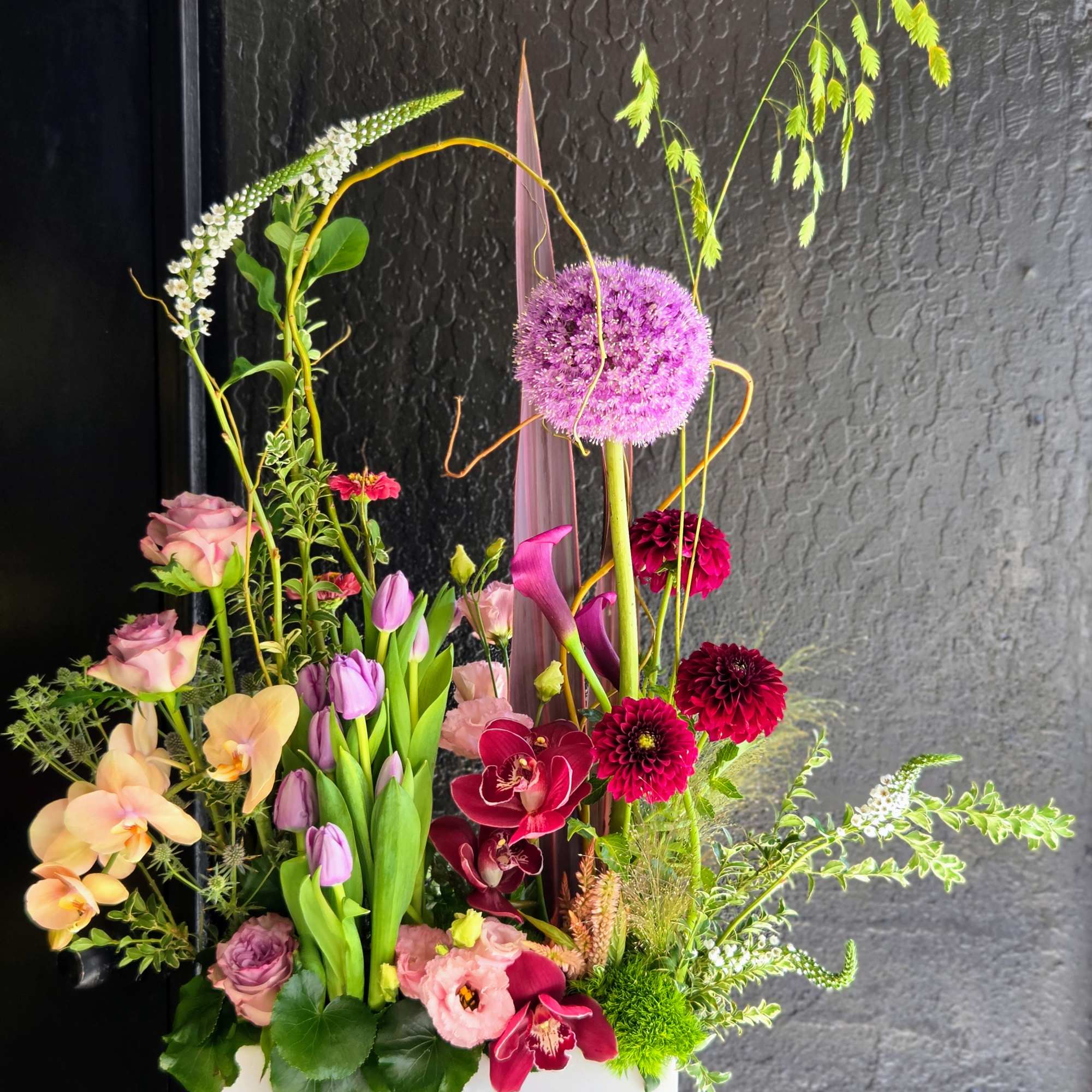 Tall mixed floral arrangement in a white rectangular vase with pink, purple, and peach blooms