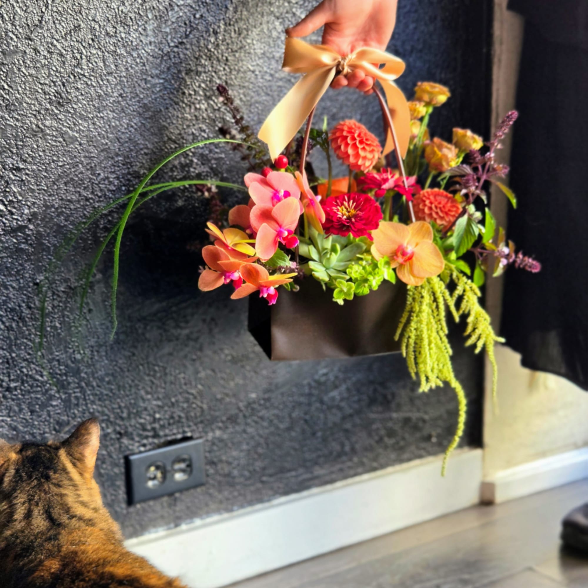 Handheld flower basket with orange and pink blooms and a satin bow