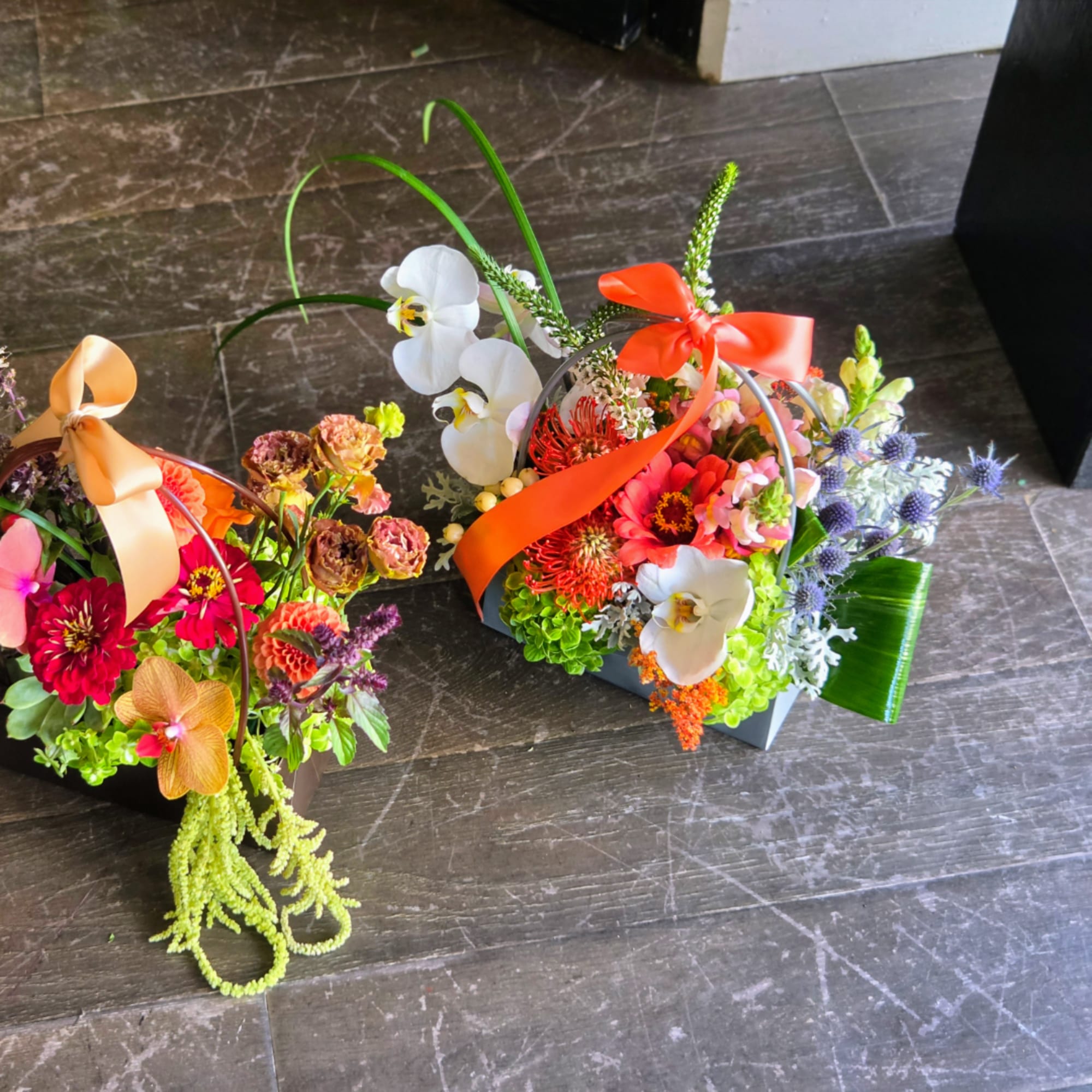 Two colorful floral basket arrangements with ribbons on a dark floor