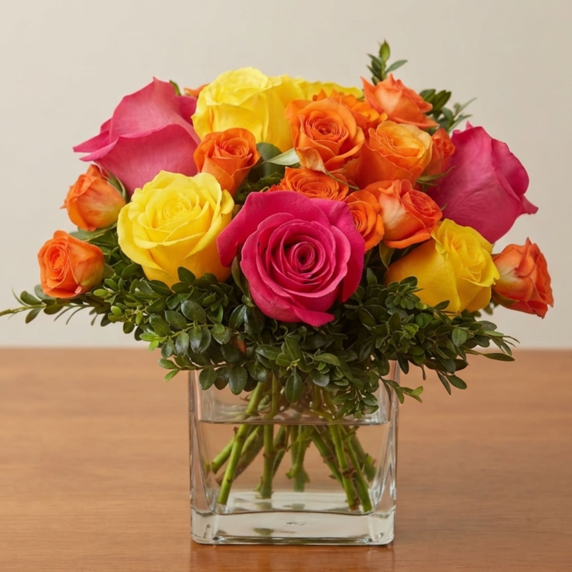 Bouquet of pink, yellow, and orange roses in a clear square vase