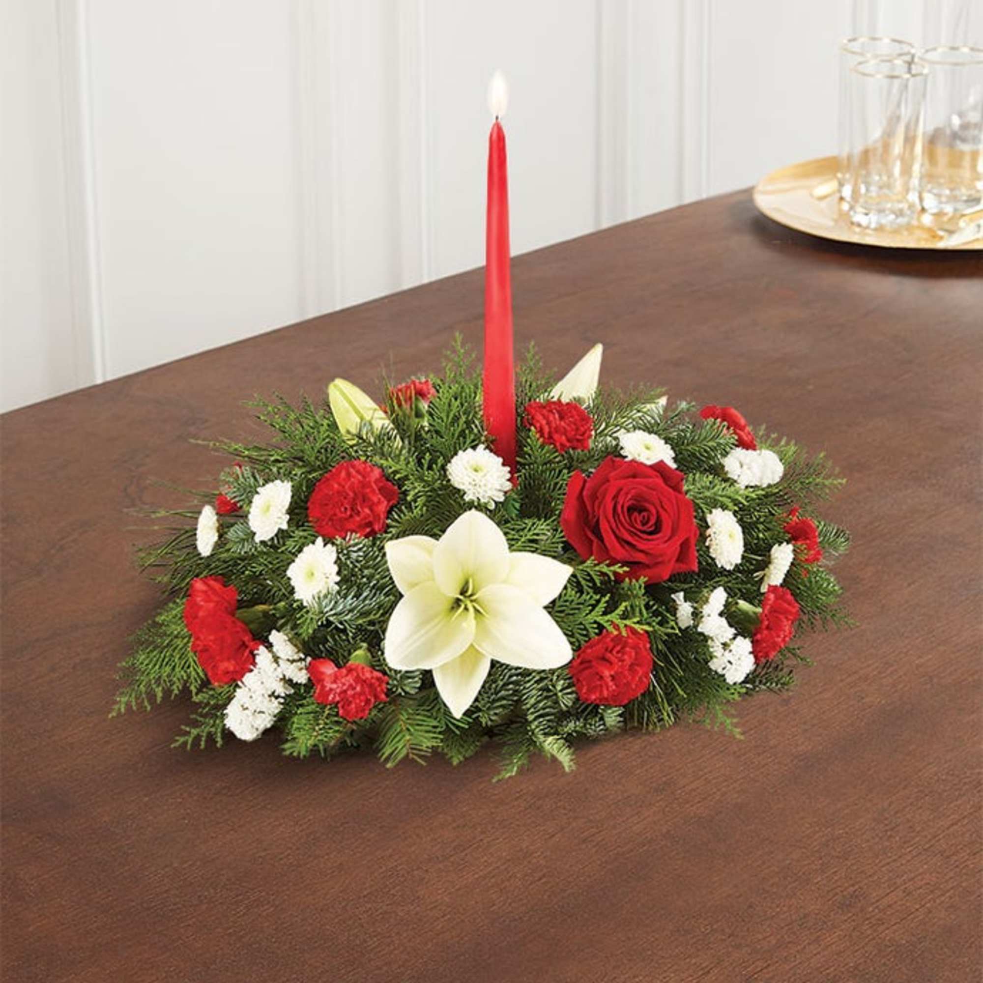 Low holiday centerpiece with red and white flowers and a red taper candle