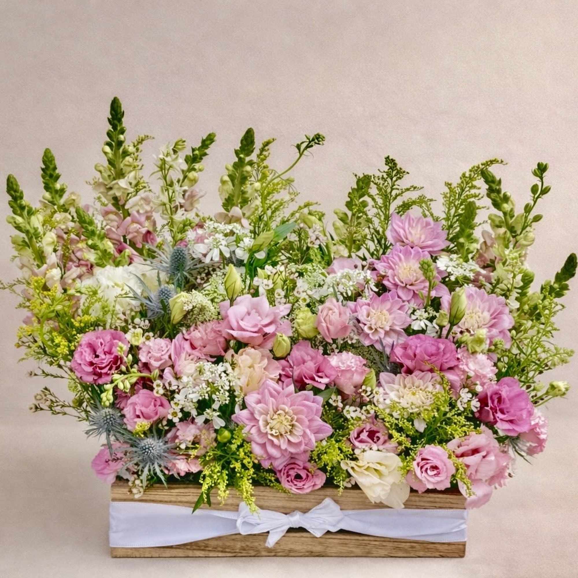 Pink and white mixed flower arrangement in a wooden box with a white ribbon