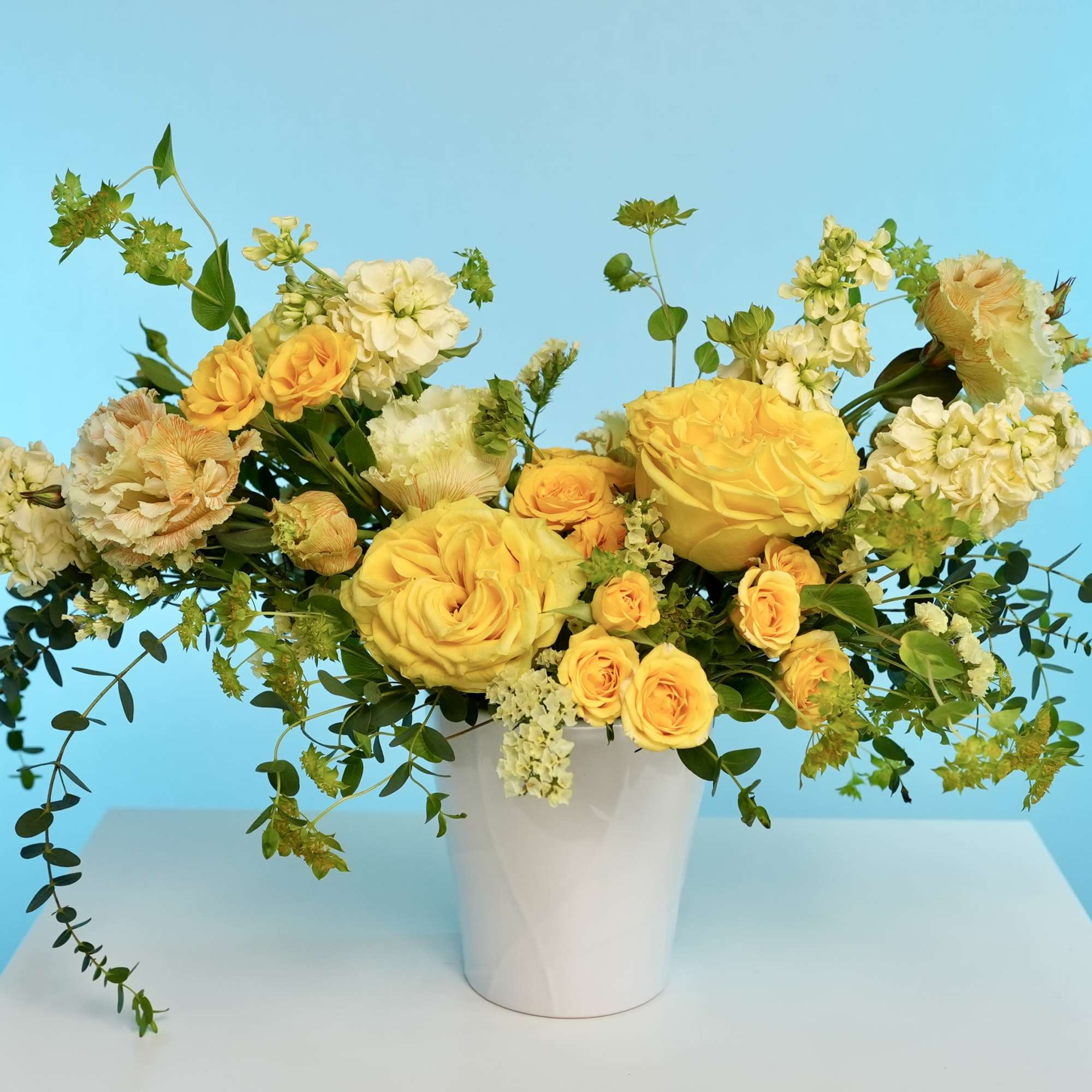 Yellow roses and cream flowers arranged in a white vase
