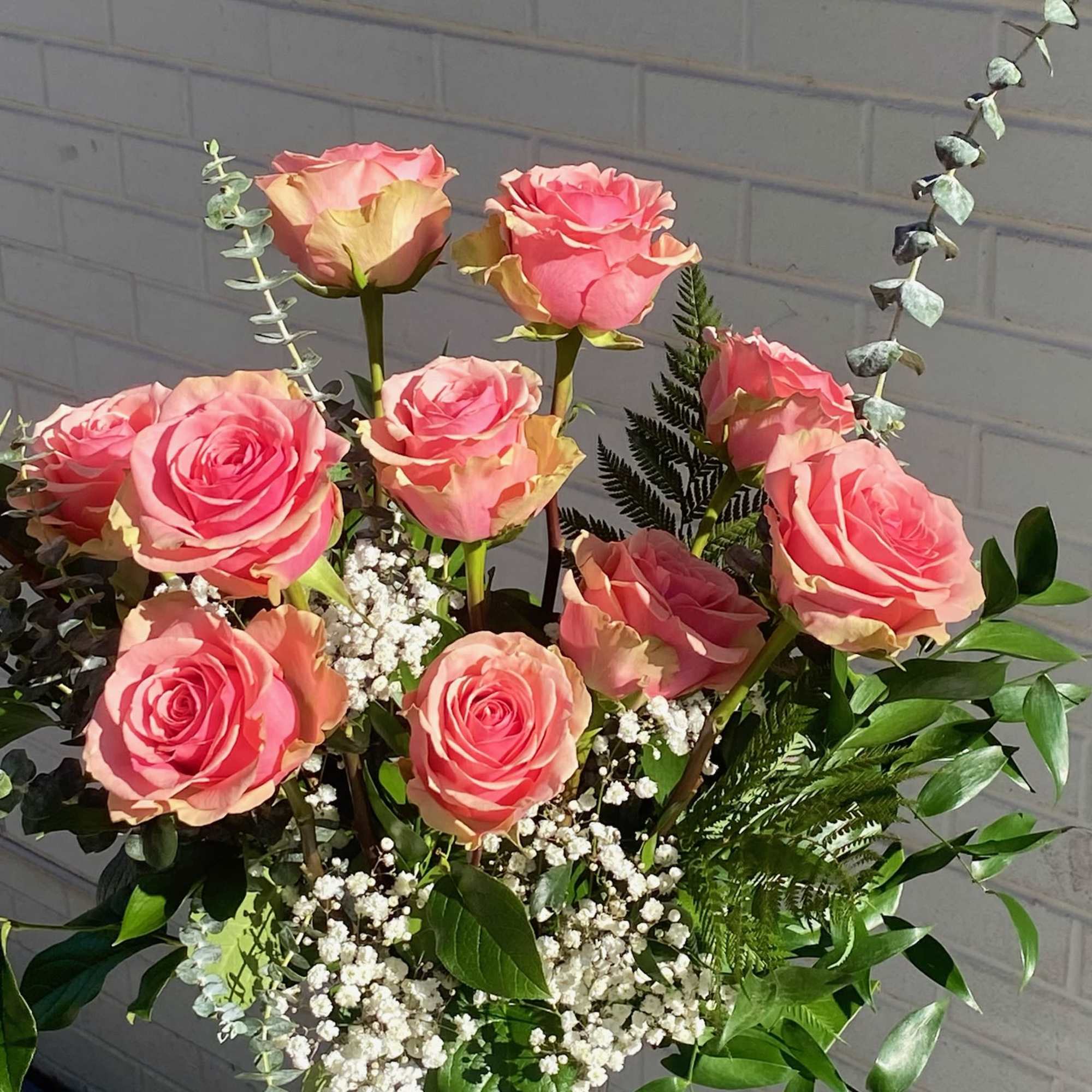 Pink roses arranged in a clear glass vase with baby's breath and greenery