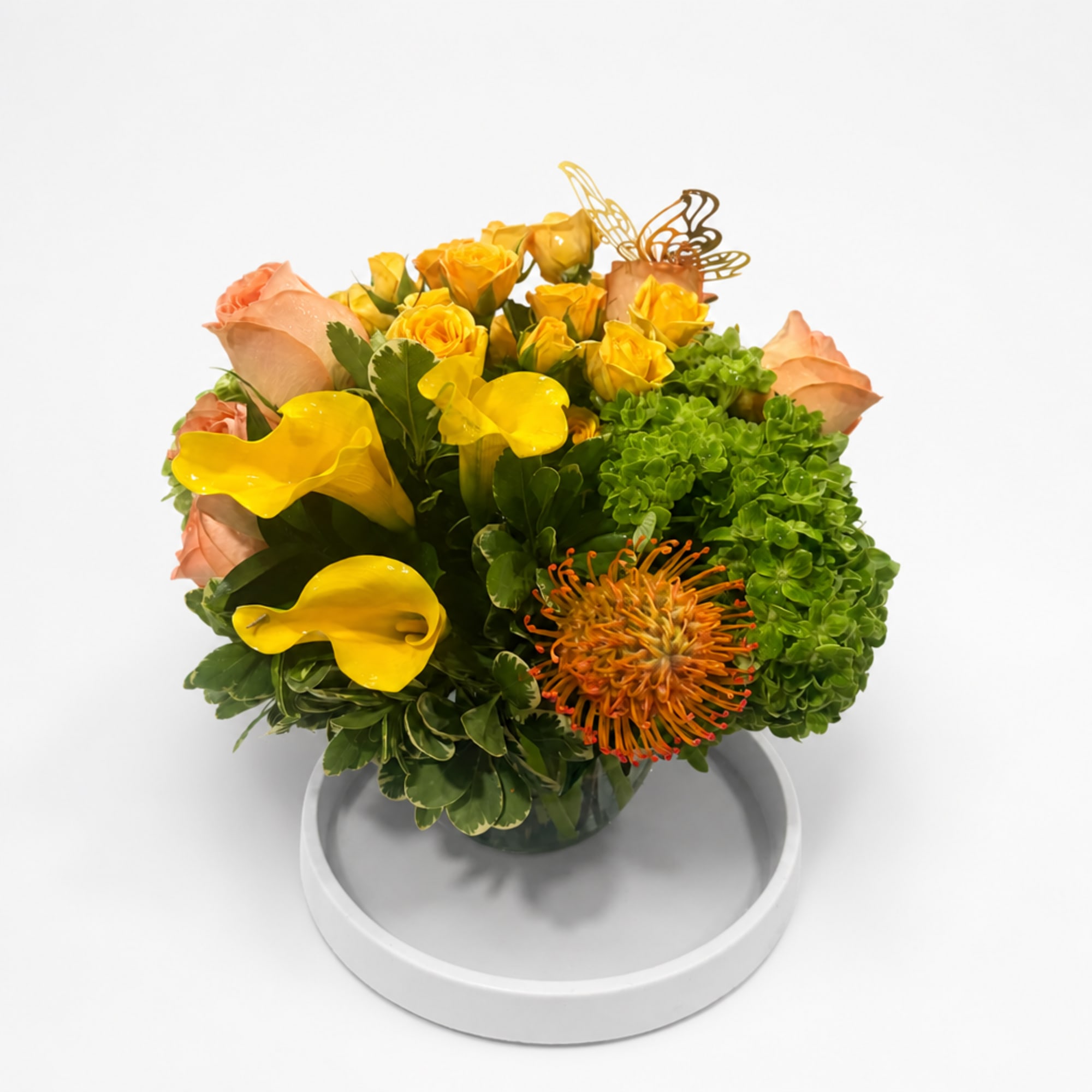 Yellow calla lilies and roses with green hydrangeas in a glass vase
